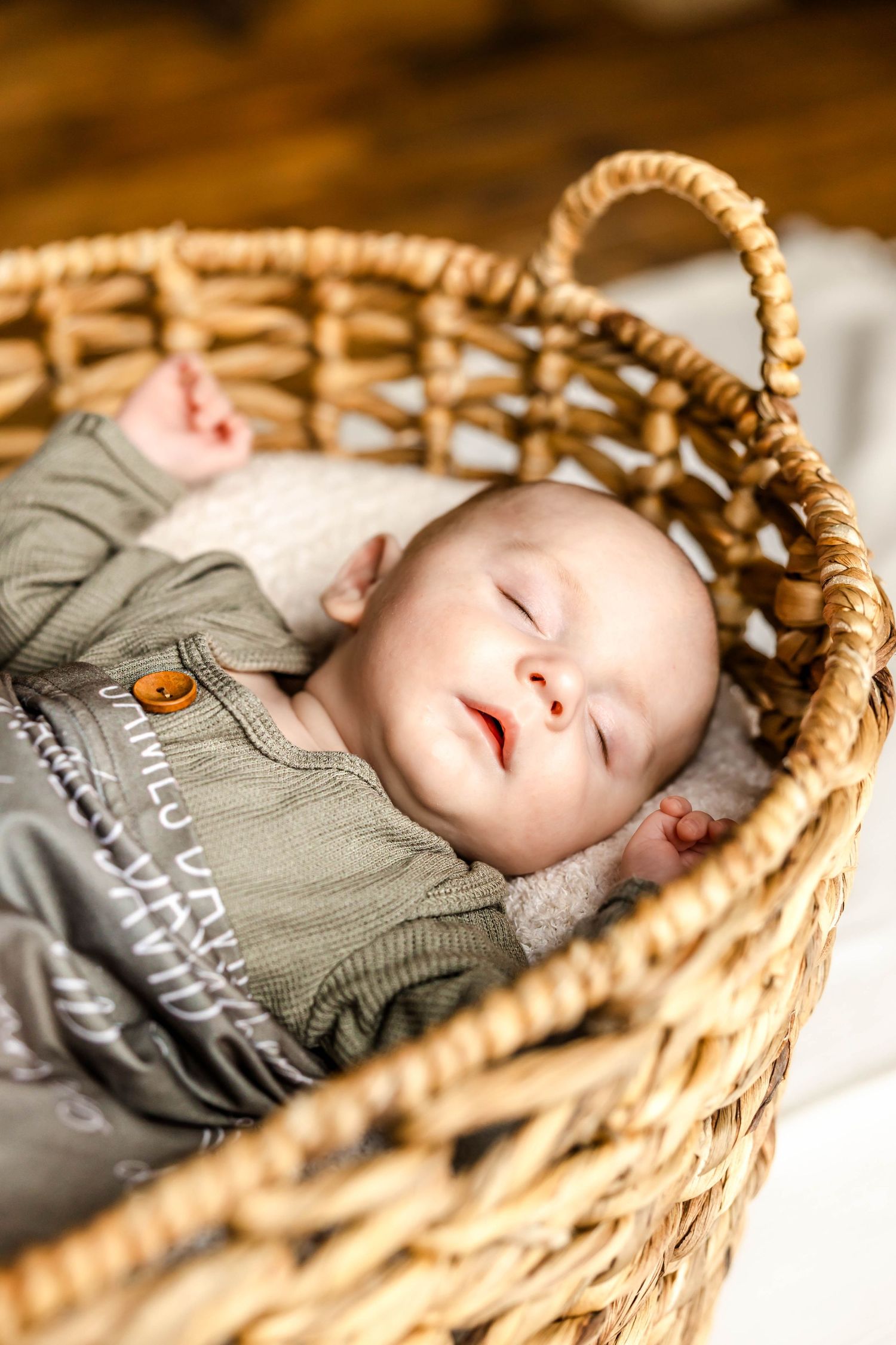 Sleeping baby rests peacefully in woven basket wearing grey outfit.
