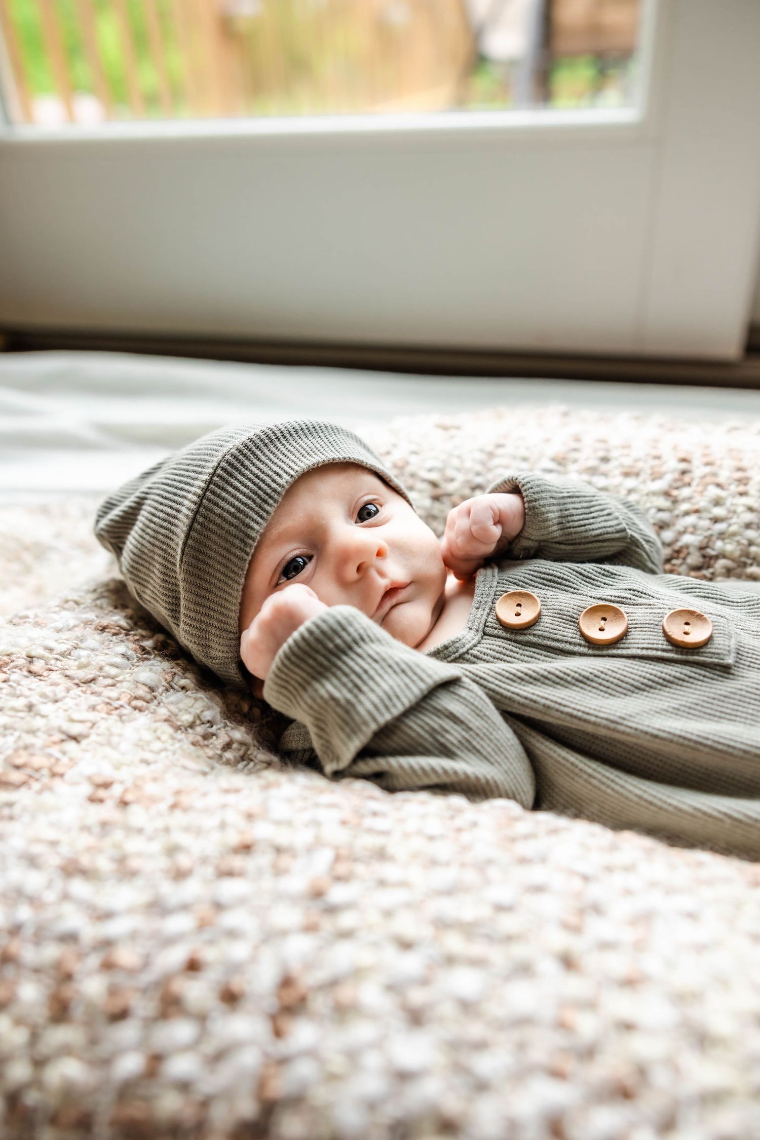 Infant wearing grey knit outfit smiling while resting on plush blanket.