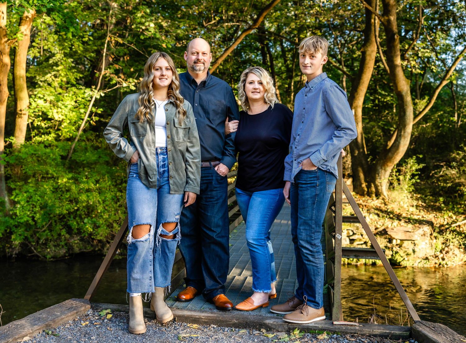 Group poses together on wooden bridge over creek during autumn photoshoot.