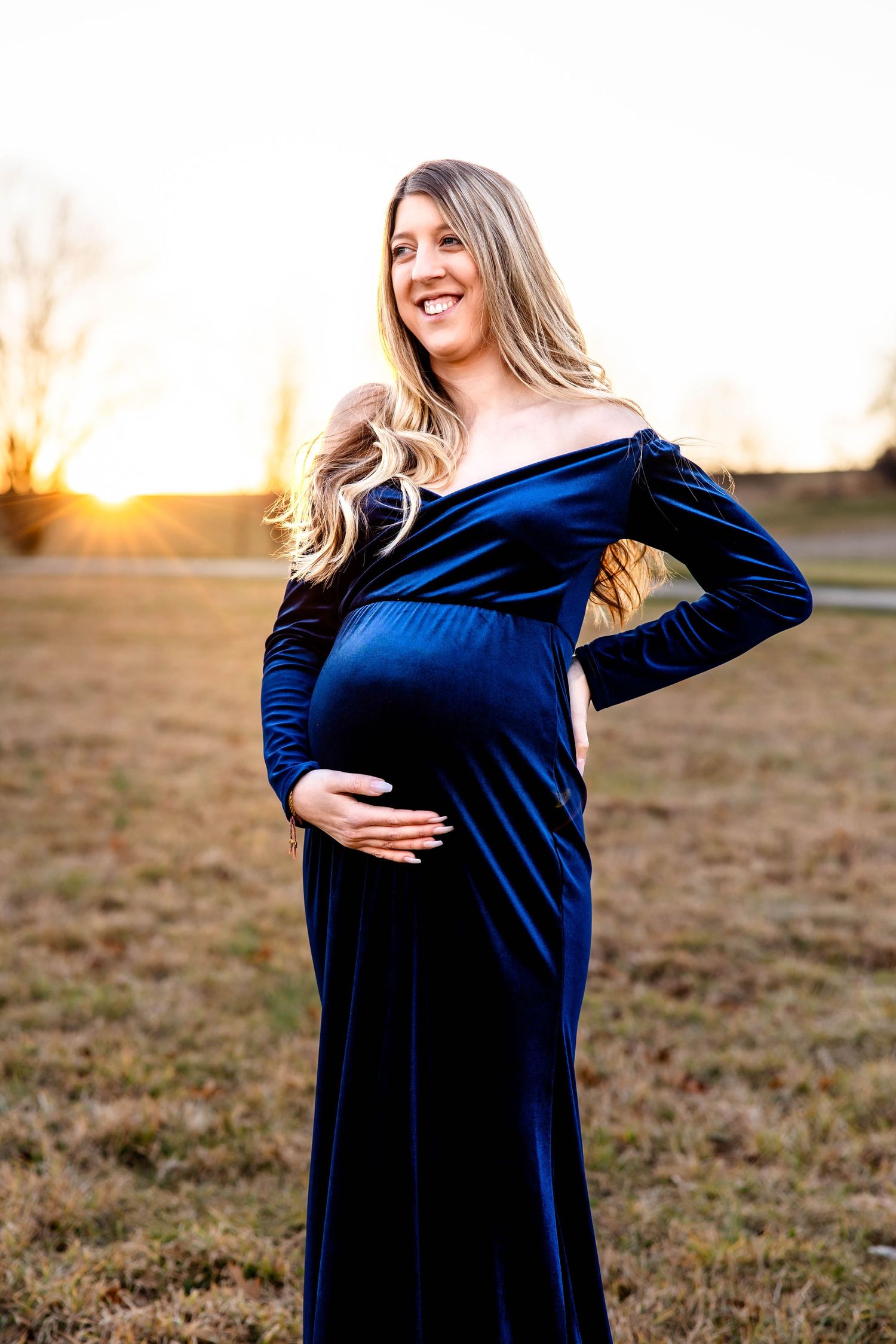 Radiant maternity photo in off-shoulder navy velvet dress at sunset.
