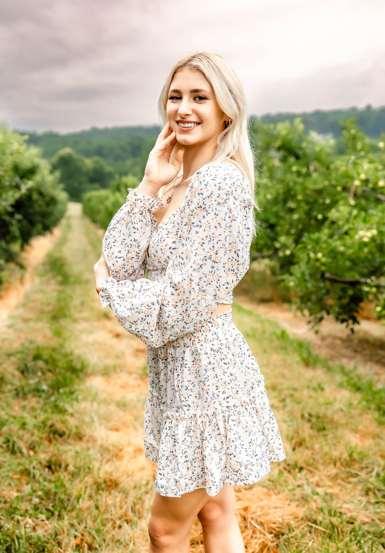 Elegant outdoor photoshoot featuring a floral print dress in a sunny orchard.