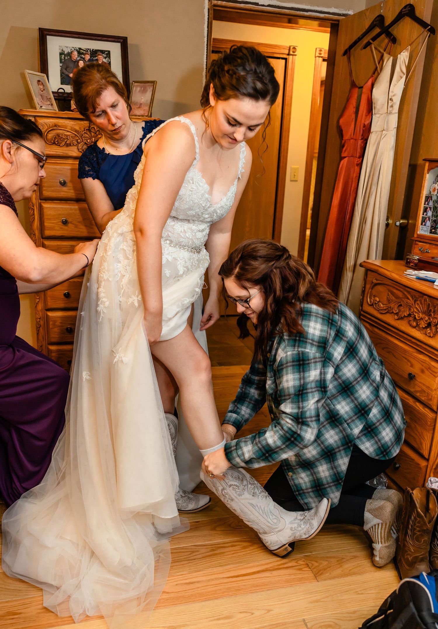 Helpers assist a bride getting dressed by adjusting her gown and shoes.