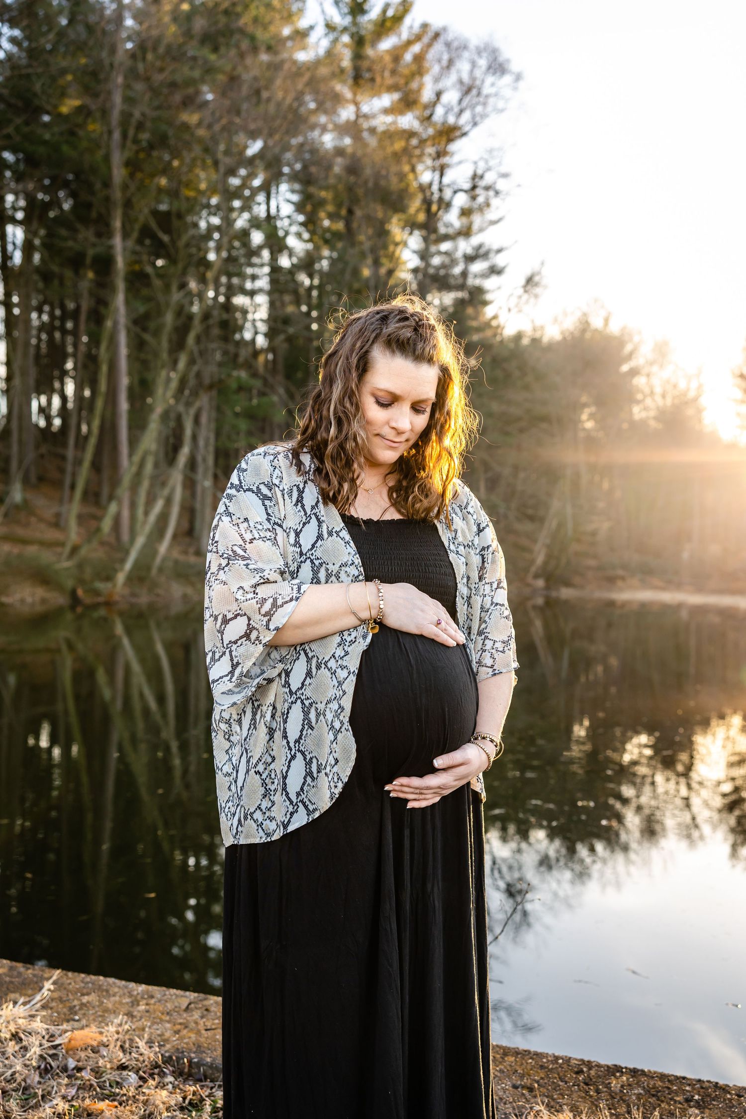 Serene maternity portrait by lake with woman in black dress and patterned kimono.
