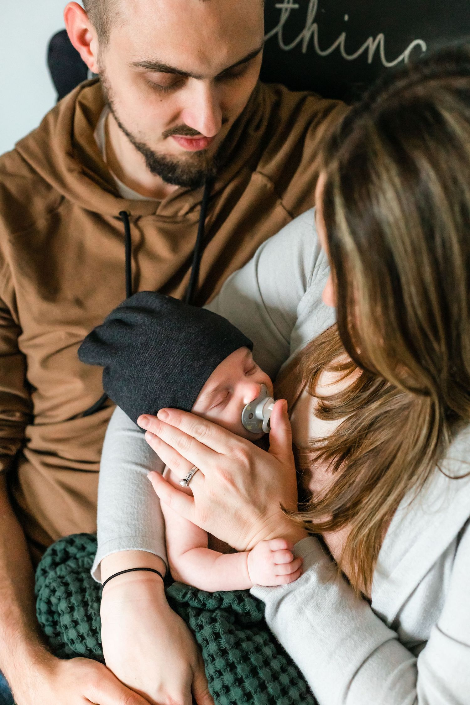 Intimate family moment with sleeping baby wearing dark hat and pacifier.