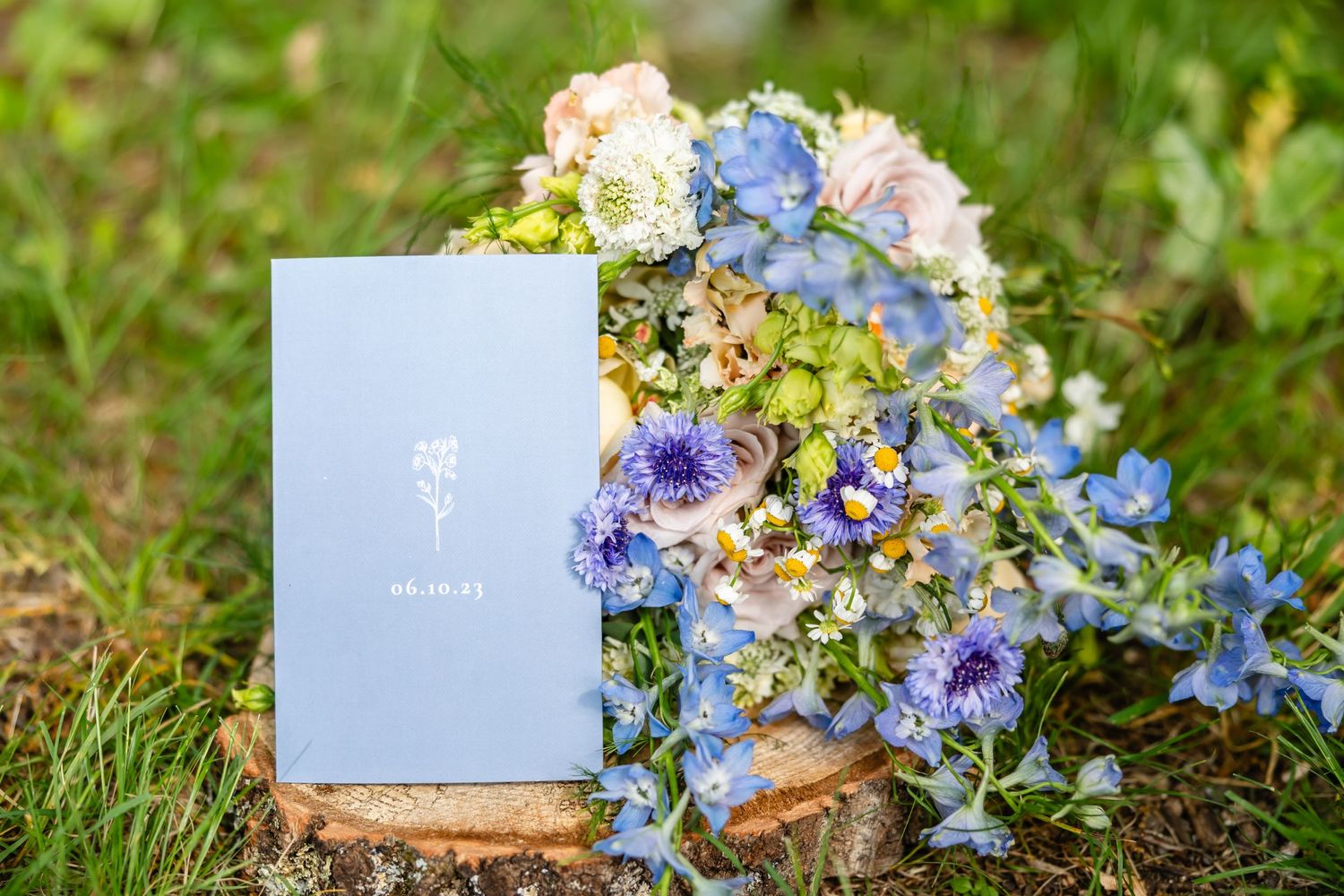 Elegant blue menu card displayed with pastel floral arrangements on grass.