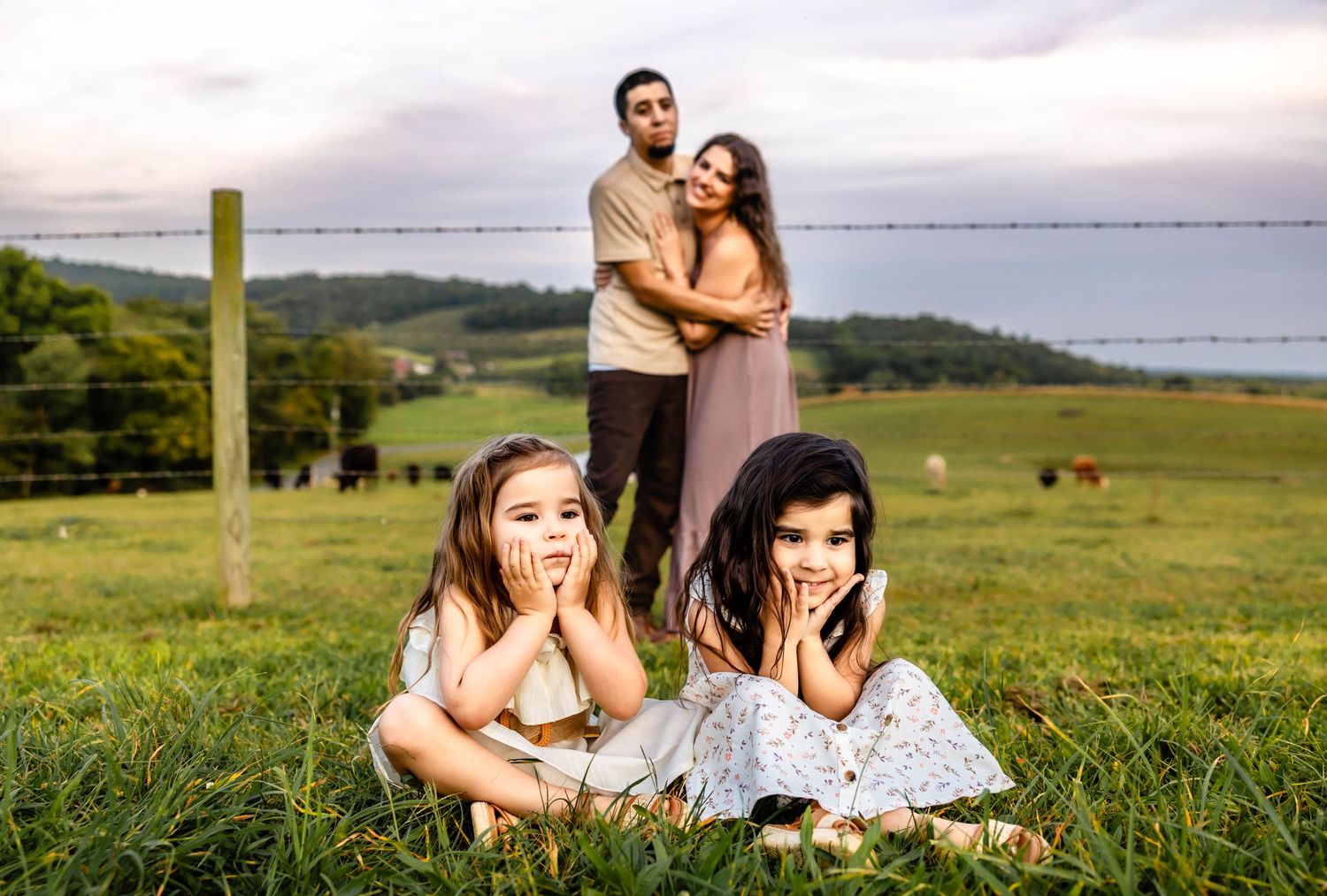 A family takes a candid photo in a pastoral setting with cattle grazing in the background.