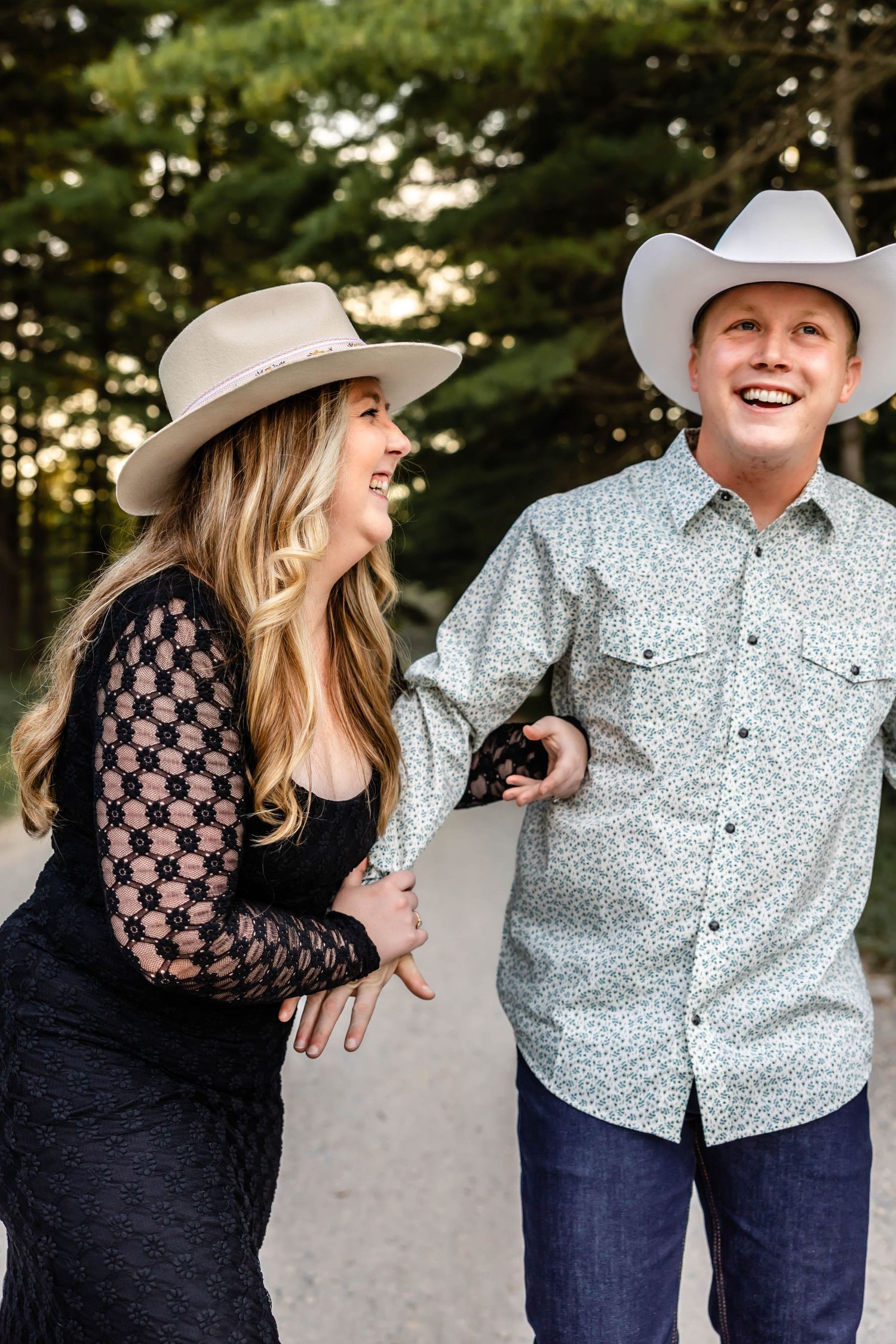 A joyful couple wearing cowboy hats share a candid laugh on a rural path.