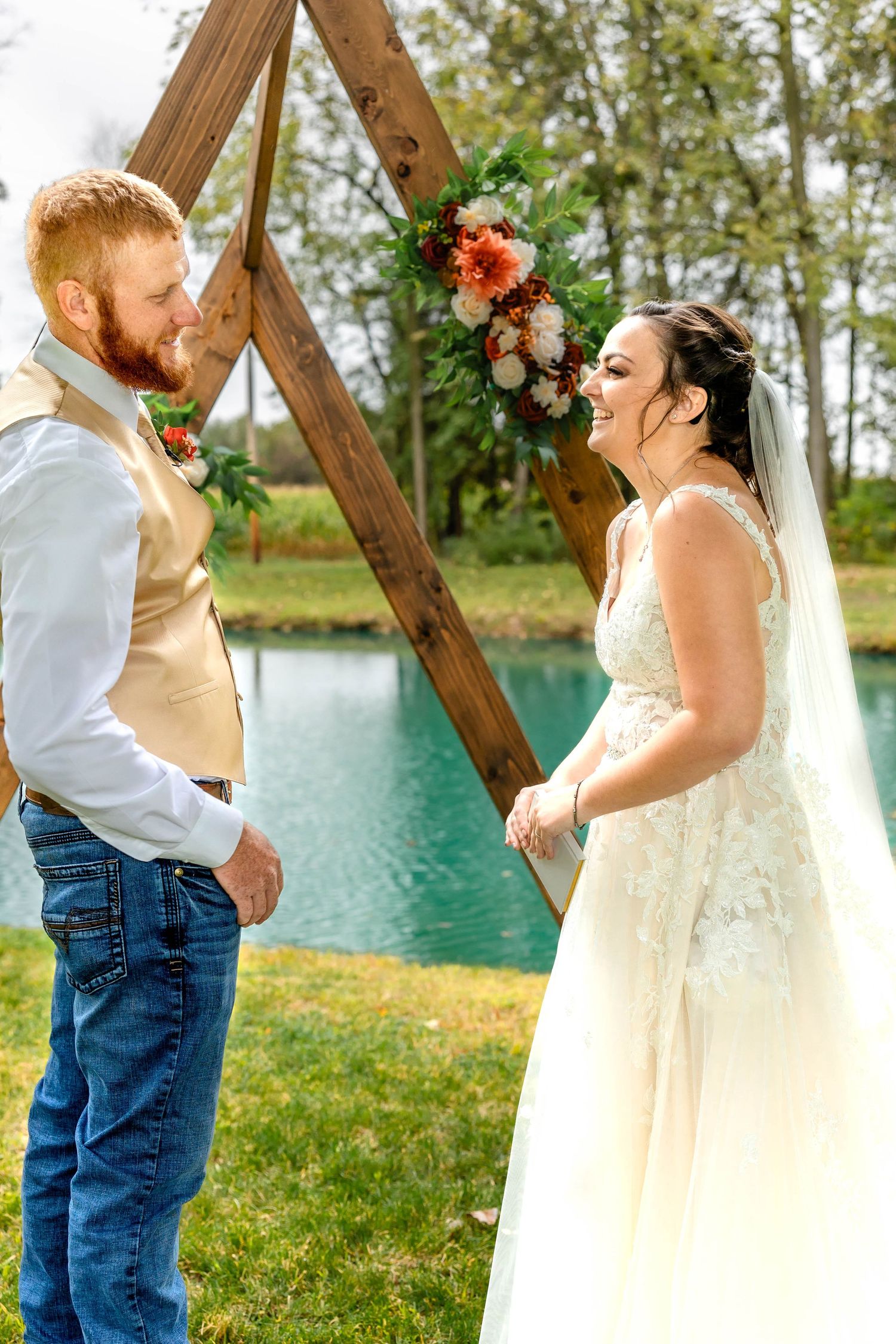 Happy couple celebrates during their wedding ceremony by a wooden triangle arch and pond.