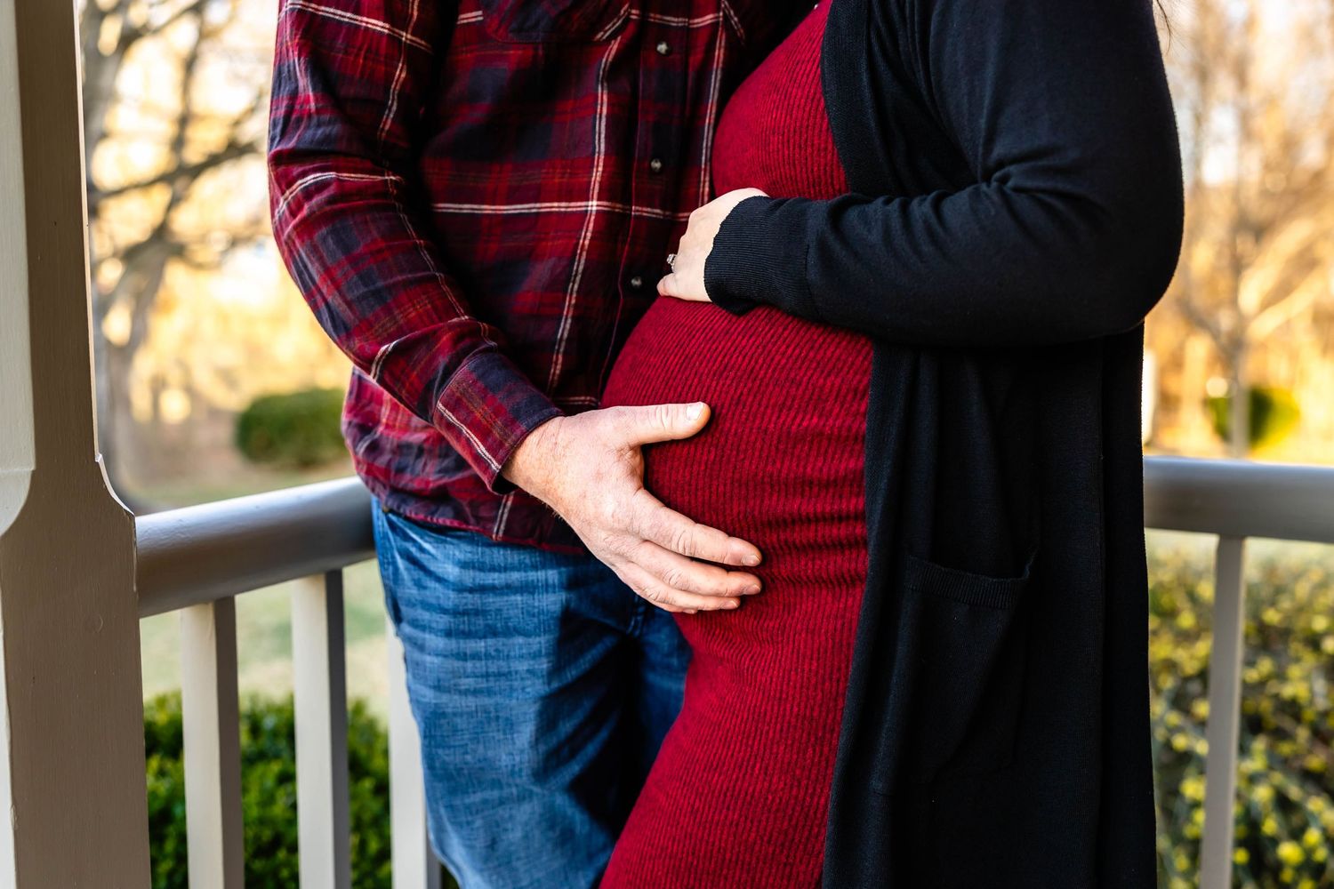 Close-up of a couple embracing with hands on a burgundy maternity dress.