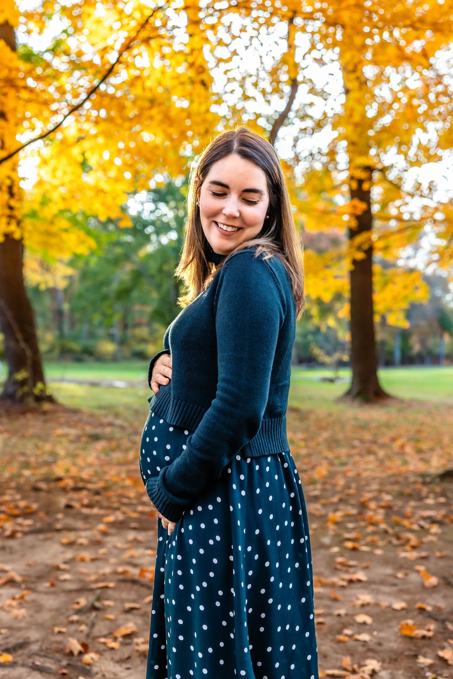 Pregnant woman in navy dress poses joyfully in autumn park setting.