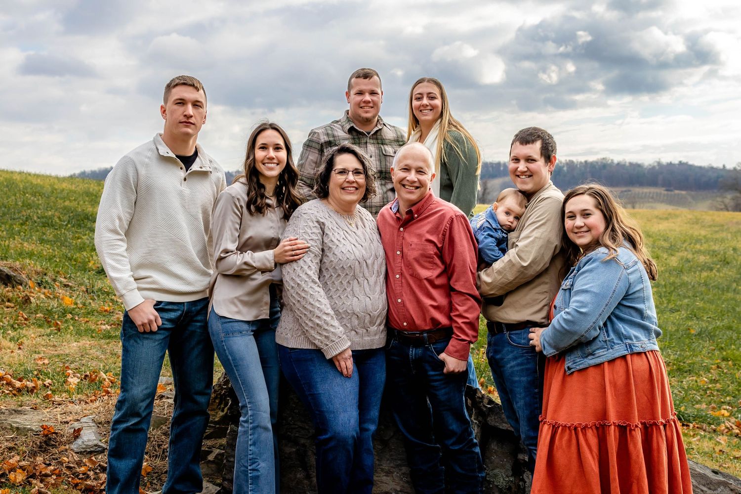 Extended family posed together on hillside during cloudy autumn day.
