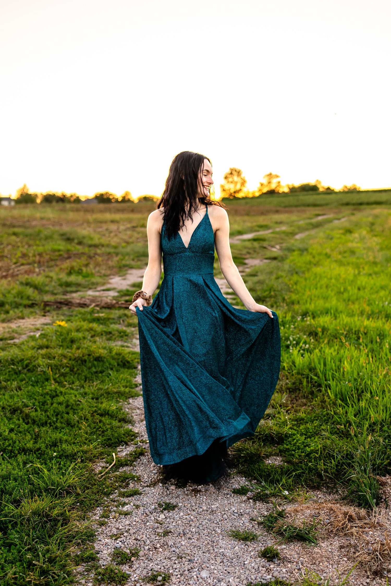 Long teal dress flows in the breeze during golden hour photoshoot in field.