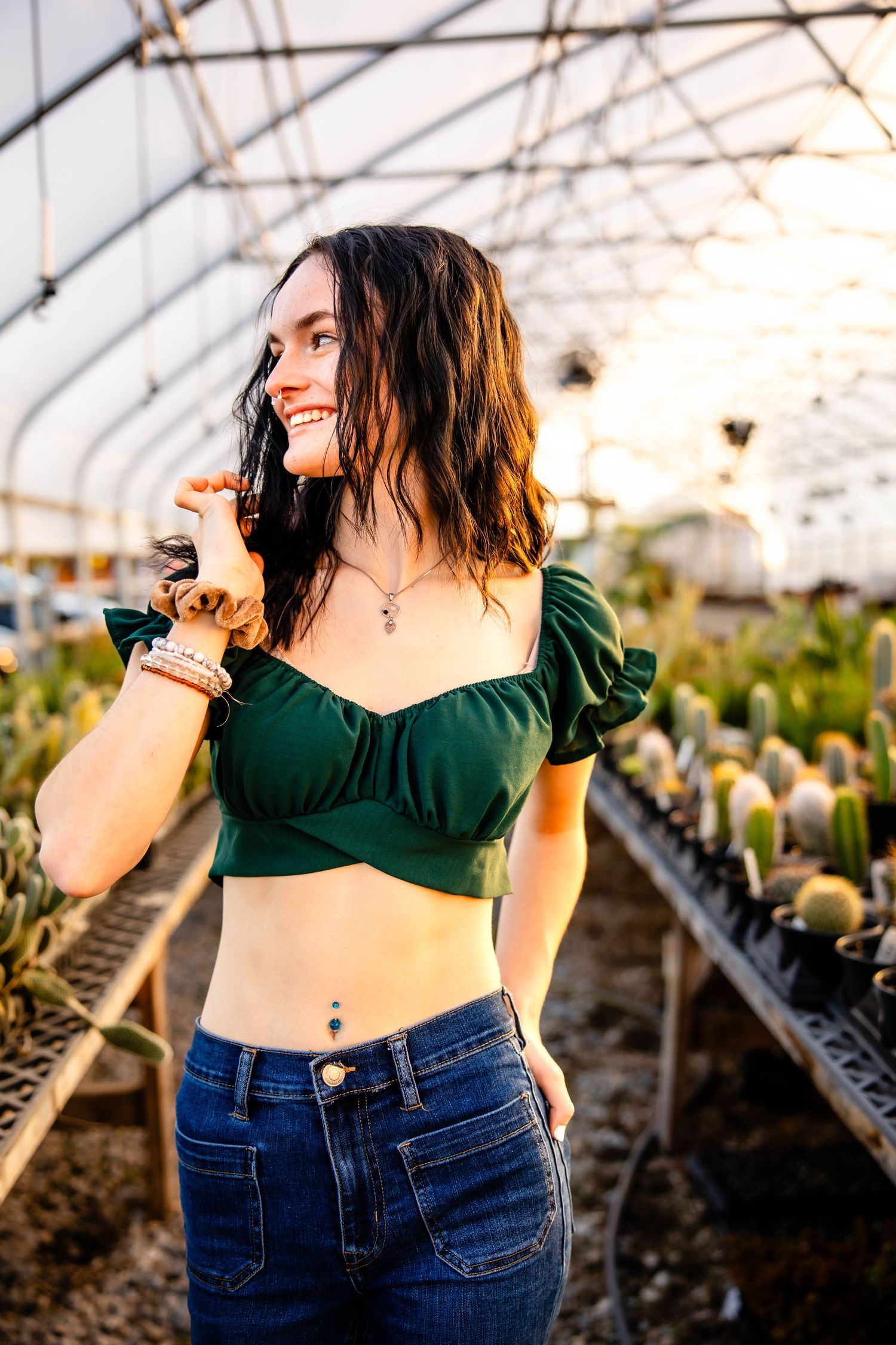 Fashion shoot in a greenhouse featuring a green crop top and high-waisted jeans against rows of plants.