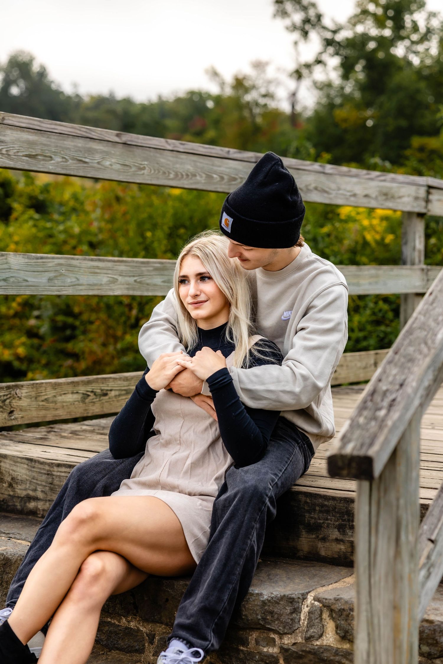 Romantic couple embraces on rustic wooden steps surrounded by autumn foliage.