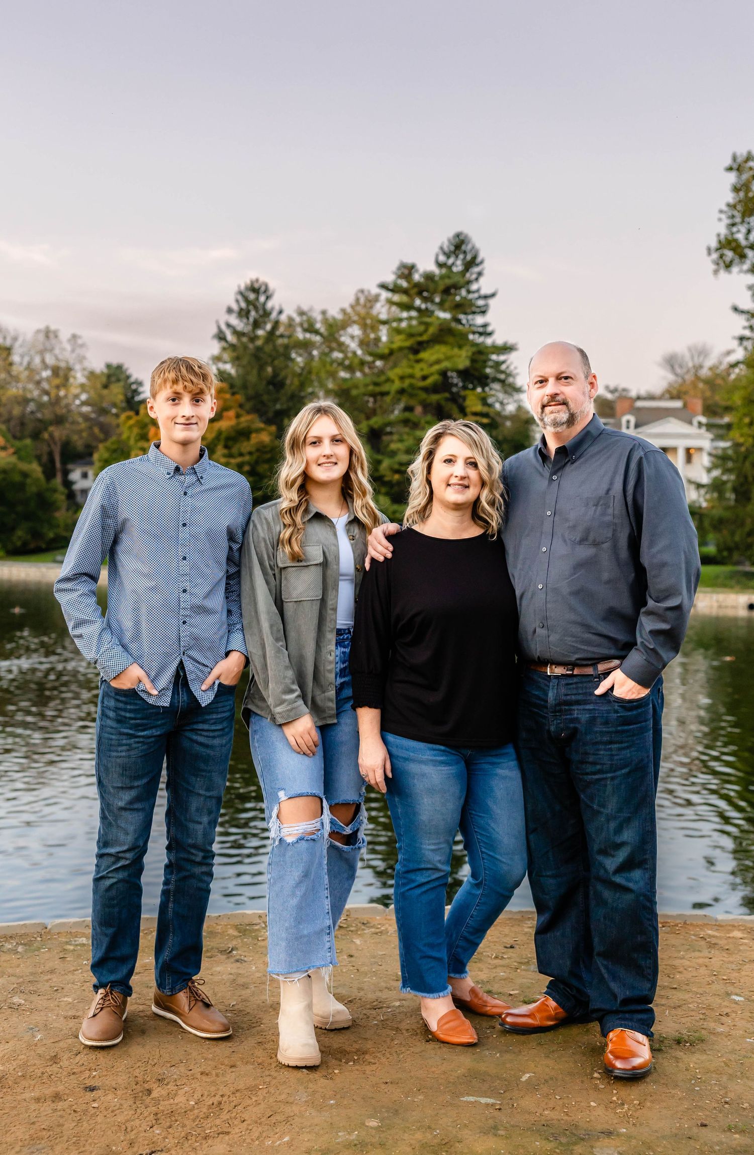 Family of four poses together by a lake during fall season.