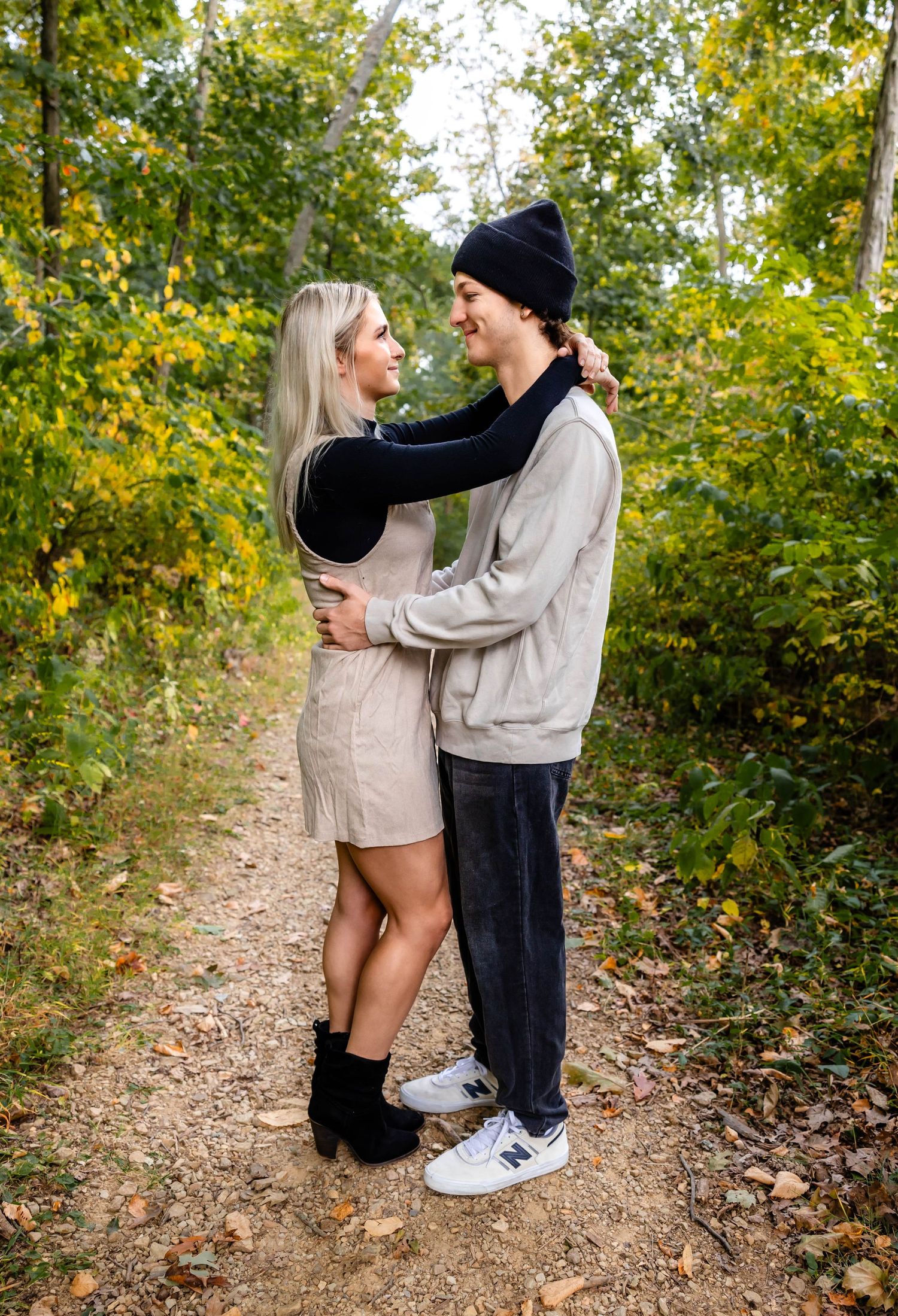 A couple embraces while standing on a dirt trail surrounded by fall foliage.
