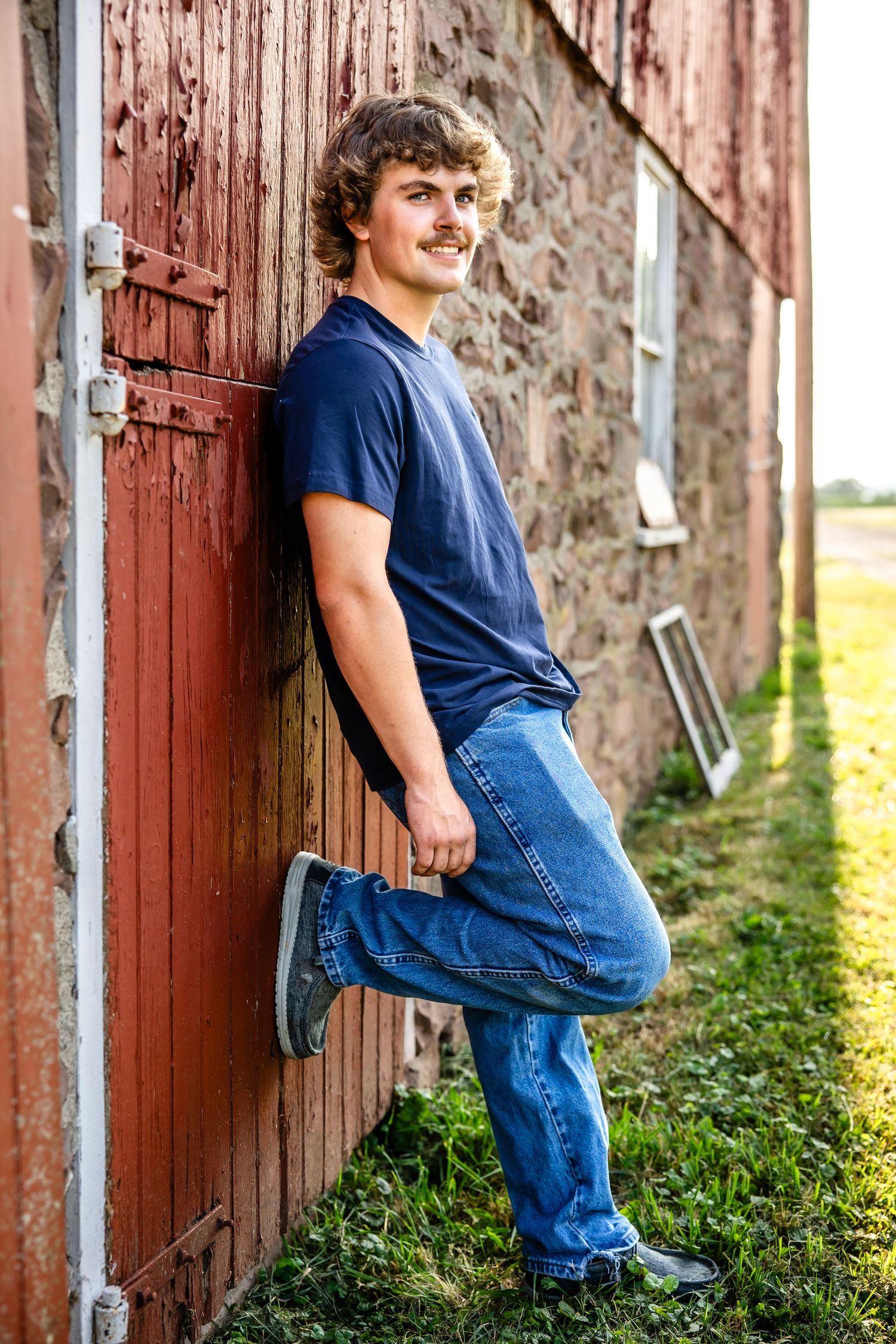 Relaxed pose against red barn door wearing casual navy shirt and denim.