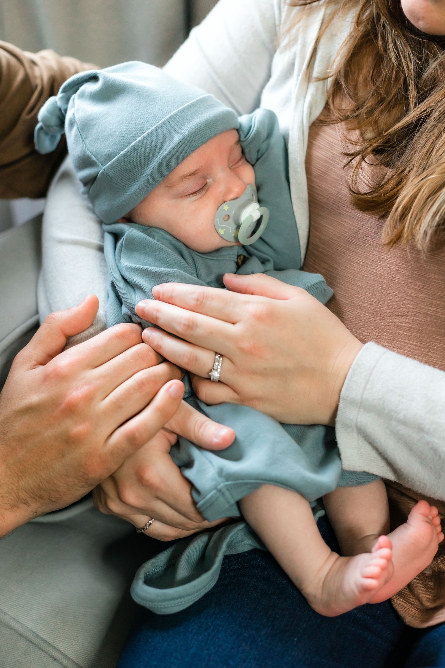 Sleeping baby in light blue outfit and hat being cradled with pacifier.