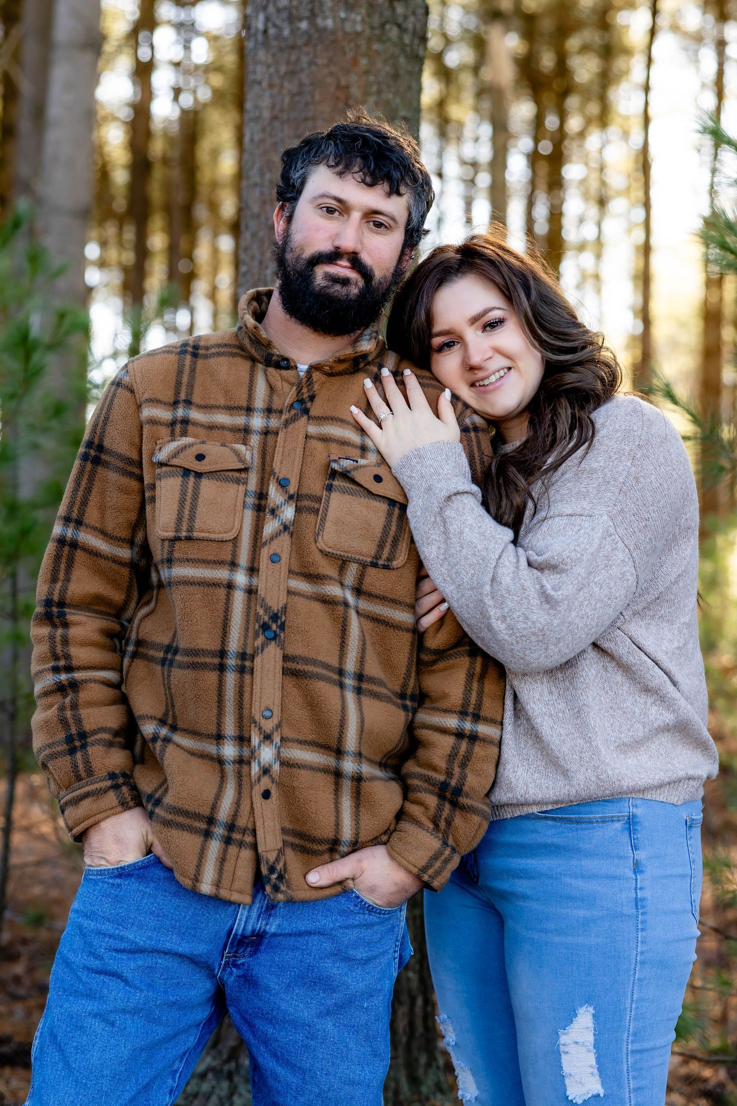 Couple in casual clothing posing together against forest backdrop.