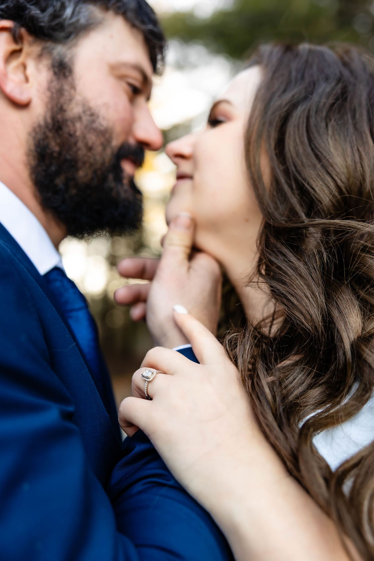 A romantic close-up of a couple about to kiss, with the person on the right showing off an engagement ring.