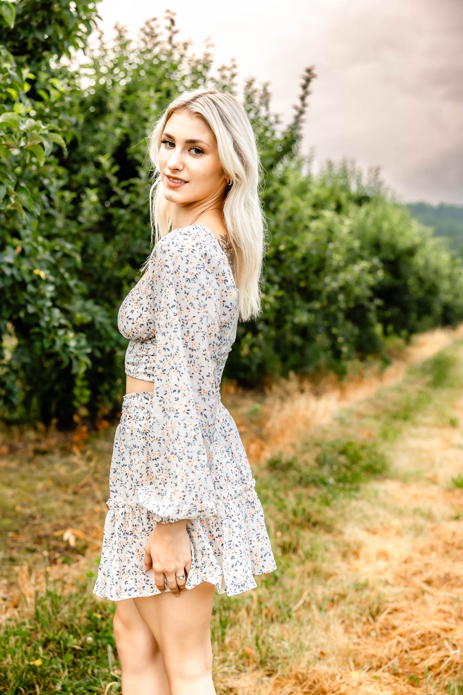 Long sleeve floral dress shown in profile against an orchard setting.