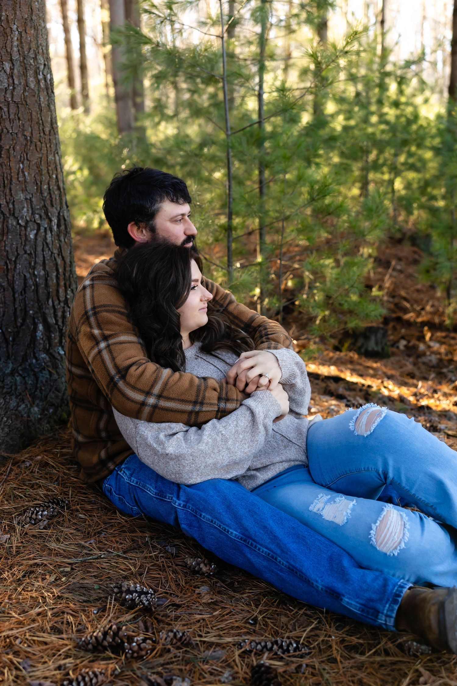 A couple shares a quiet moment together while sitting on pine needles in a forest setting.
