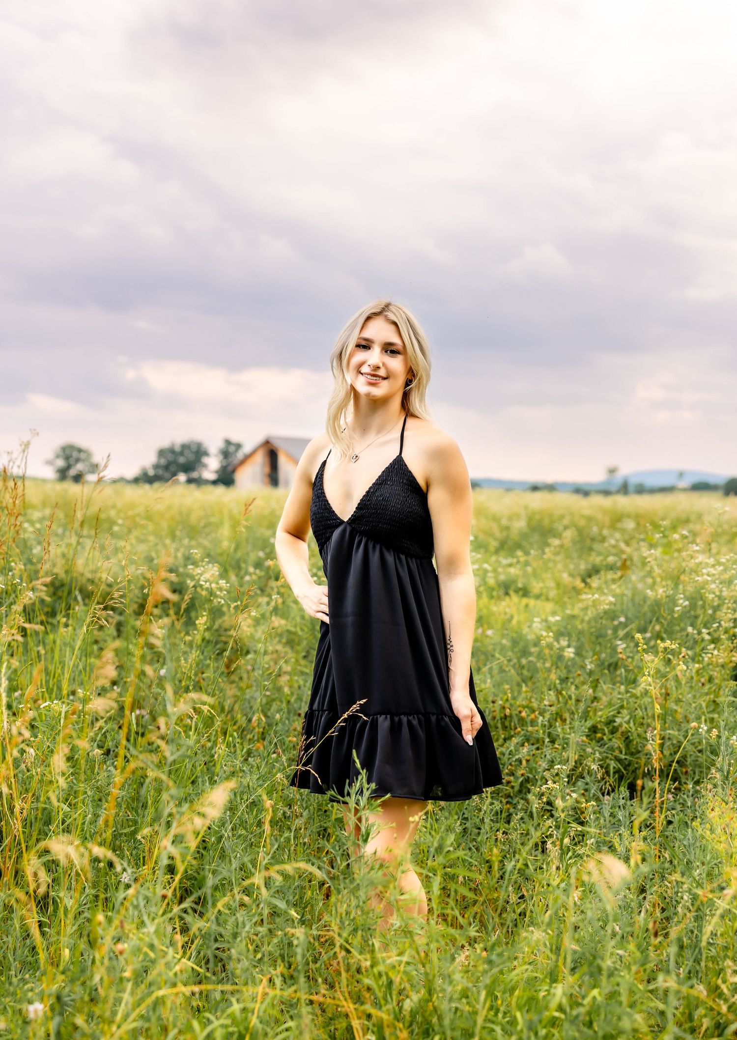 Summer portrait in black sundress standing in wildflower field under cloudy sky.