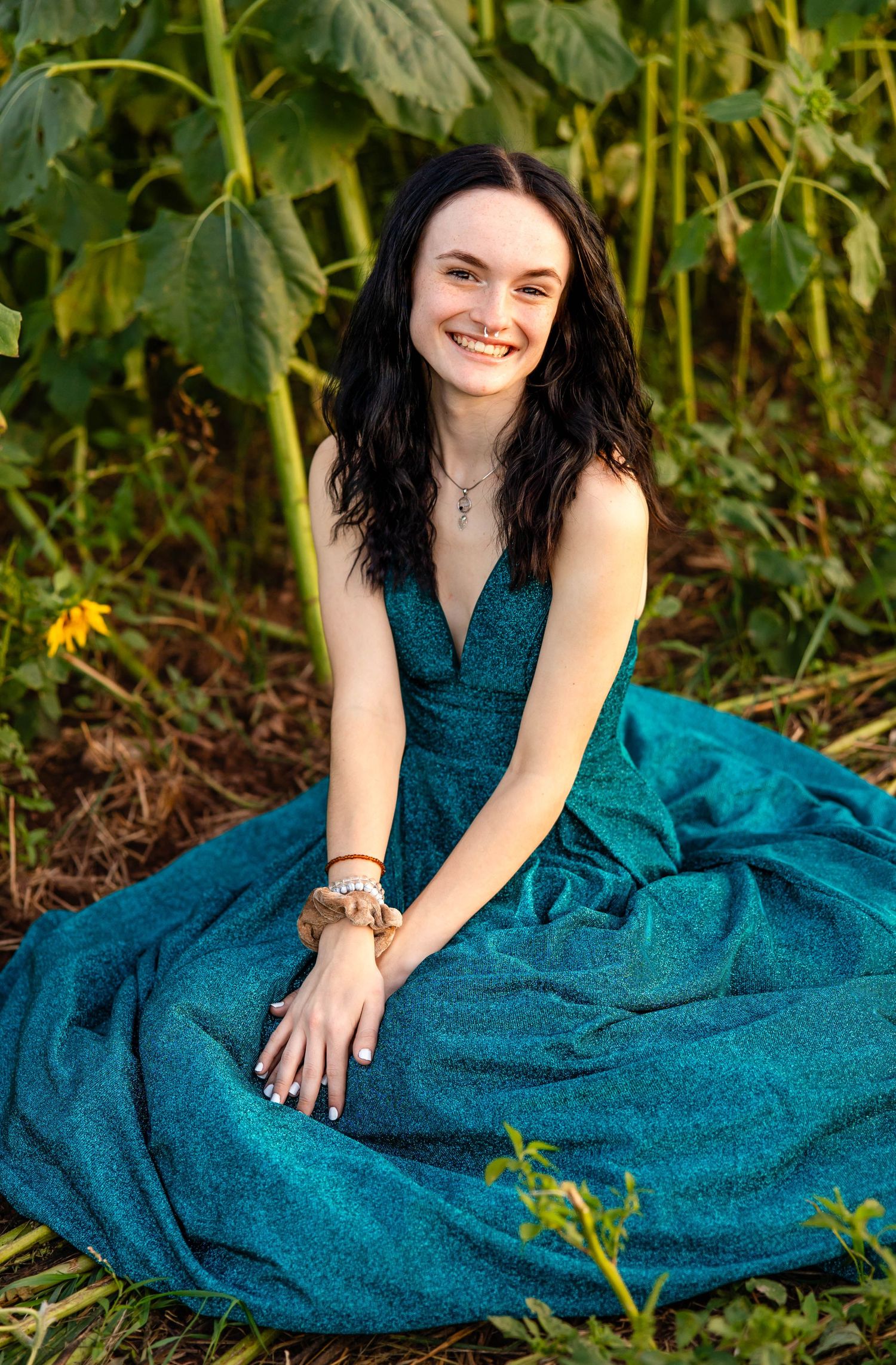 Outdoor portrait session in flowing teal evening gown surrounded by garden foliage.