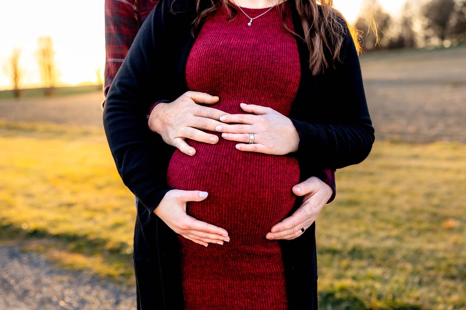 Close-up of hands cradling pregnant belly in burgundy dress.