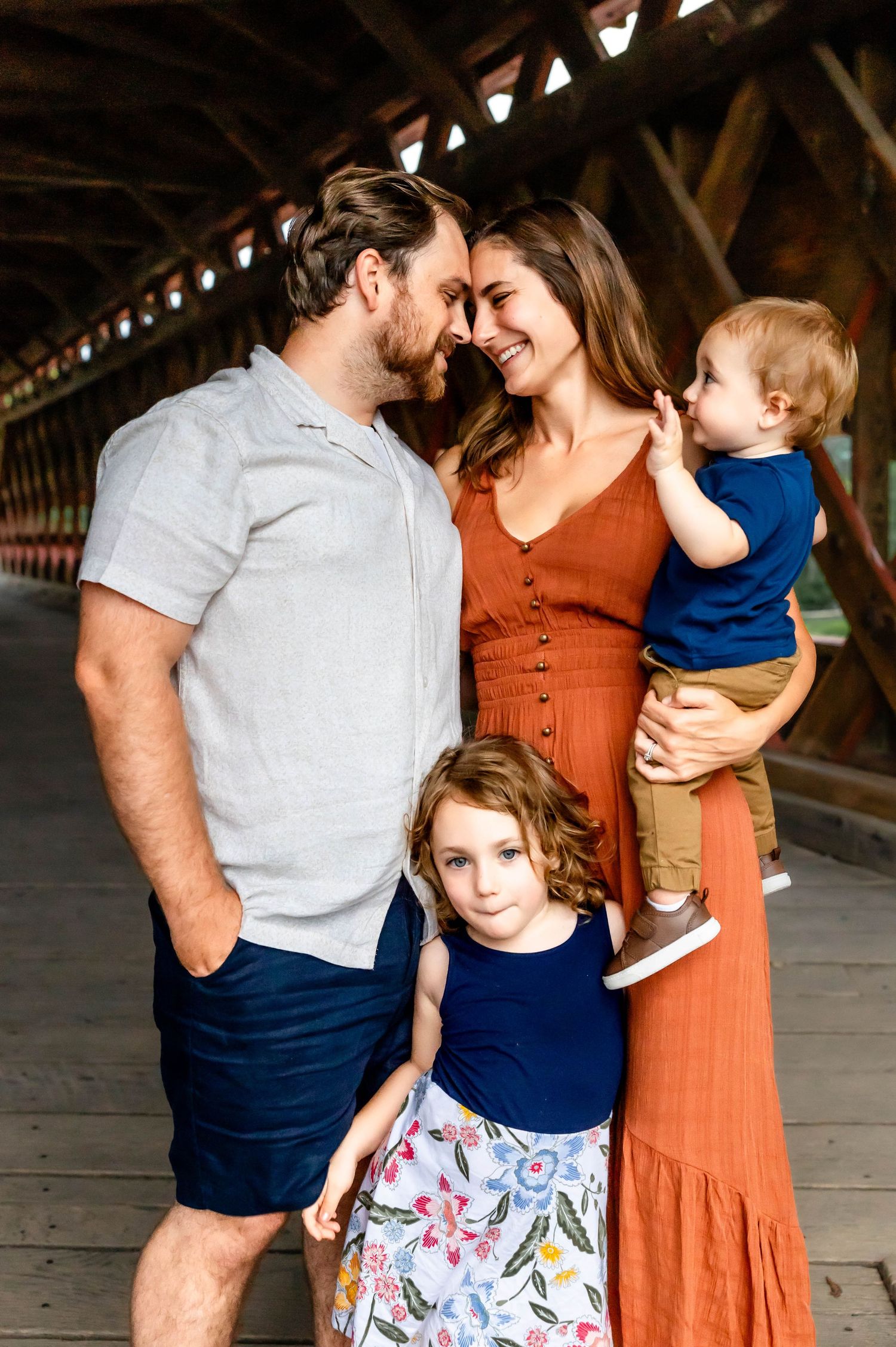 A family of four shares an intimate moment together in a rustic covered bridge setting.