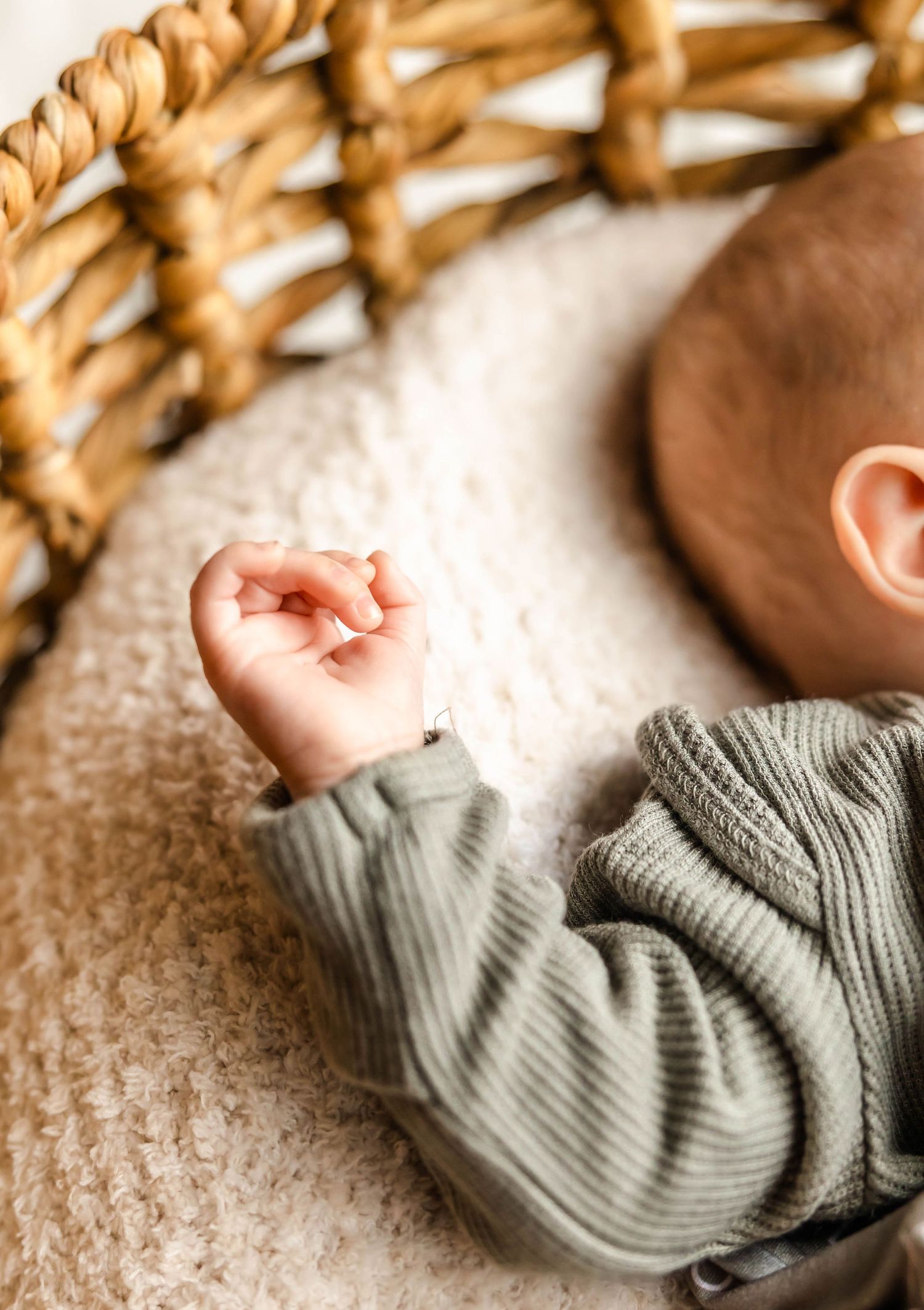 Infant wearing gray sweater rests beside woven basket detail.