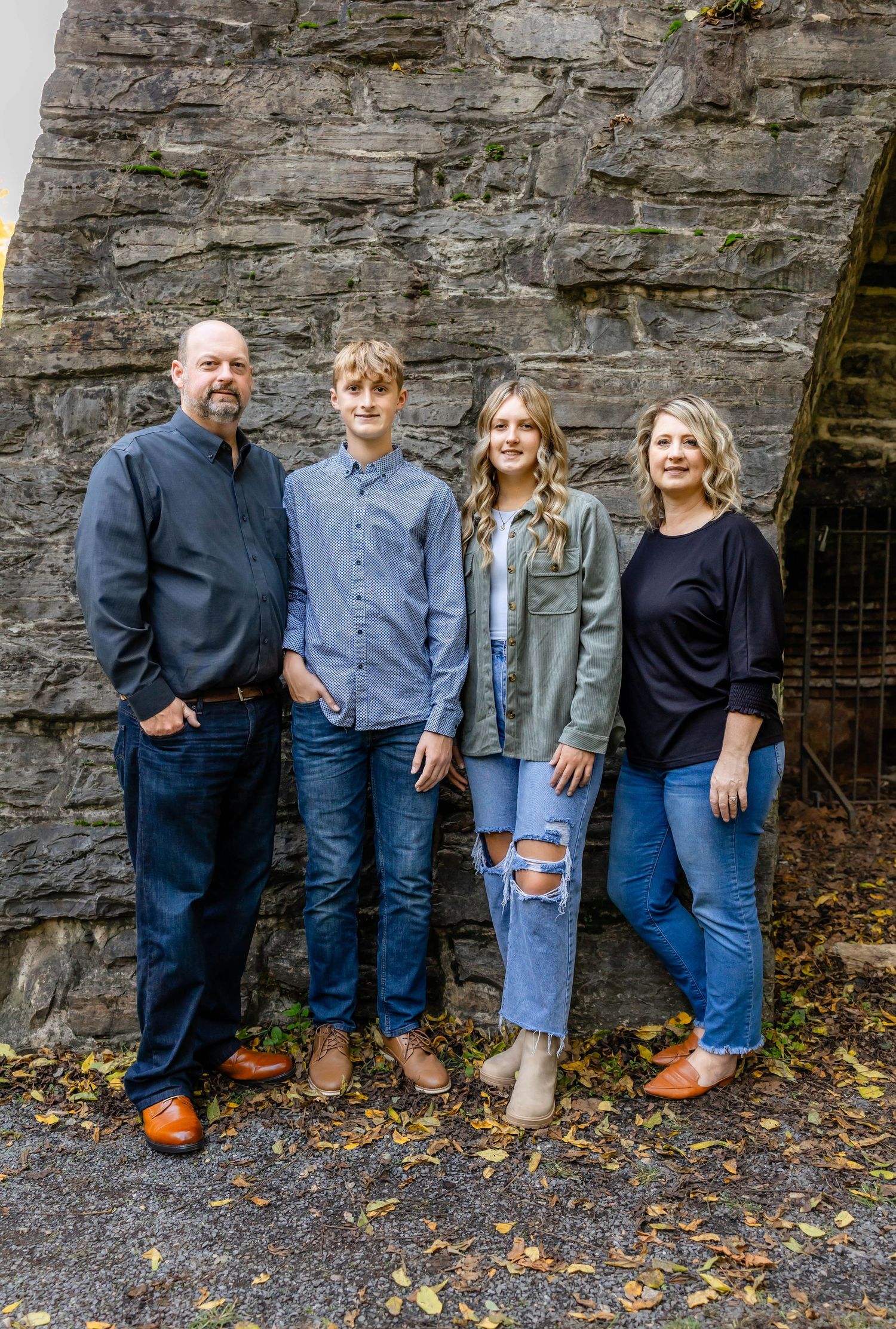 A family stands together against a textured stone wall backdrop outdoors.