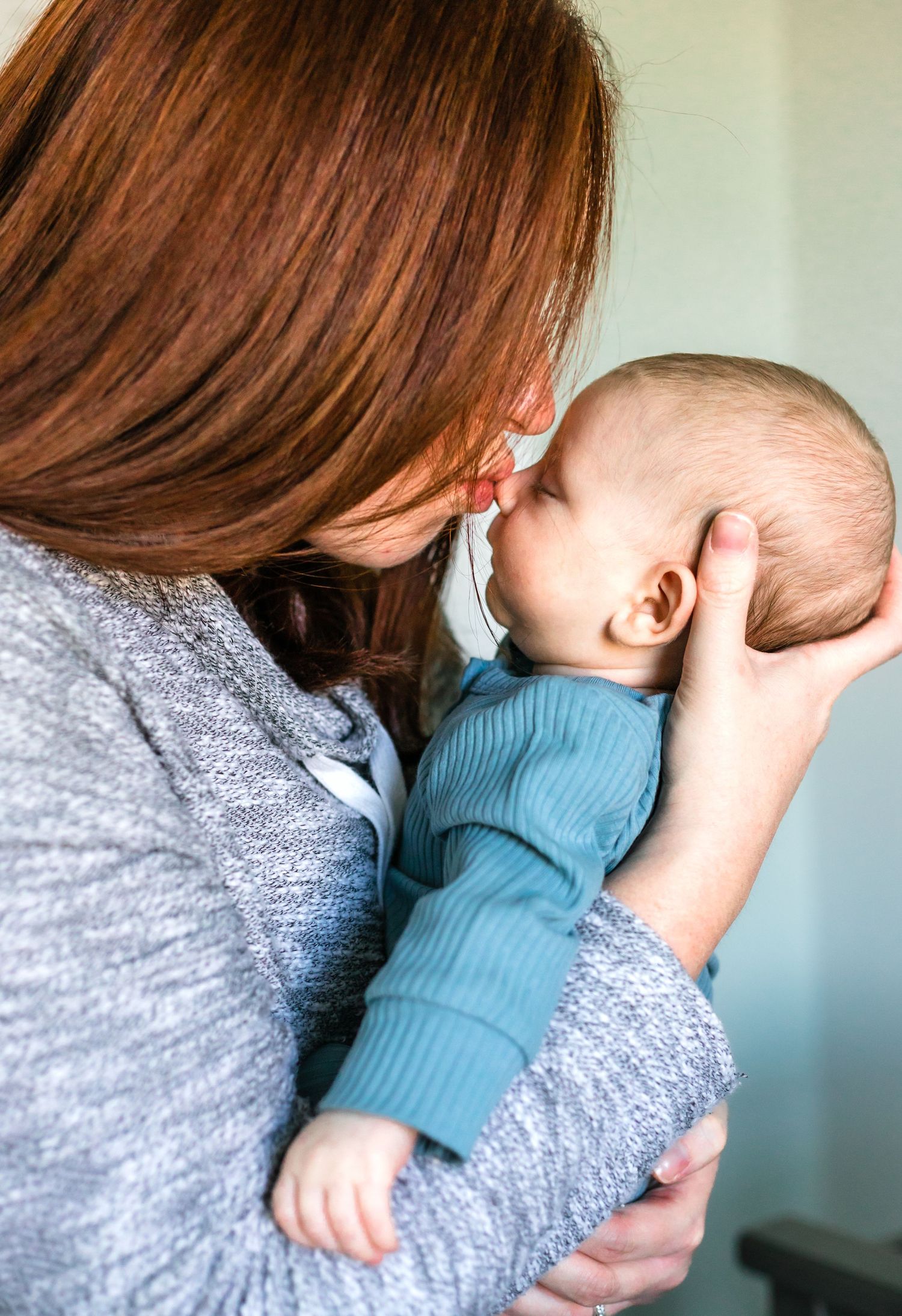 Close-up of parent in gray sweater cradling and kissing a baby in blue.