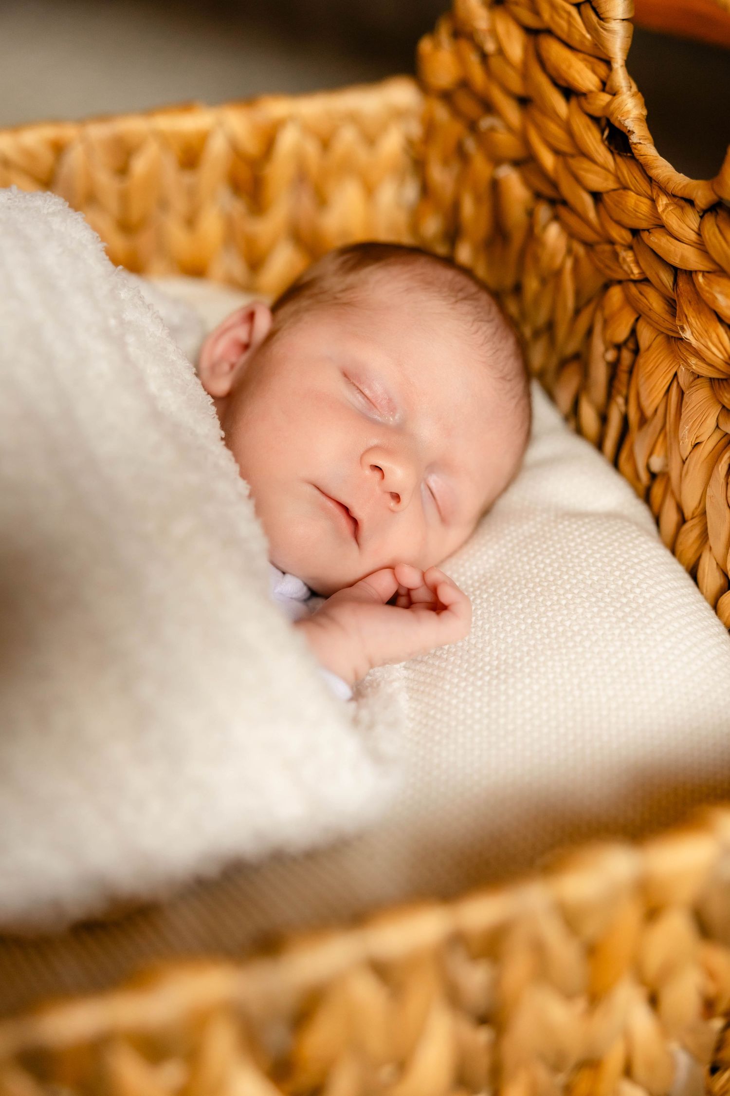 Peaceful newborn baby sleeping in a woven basket wrapped in soft white blankets.