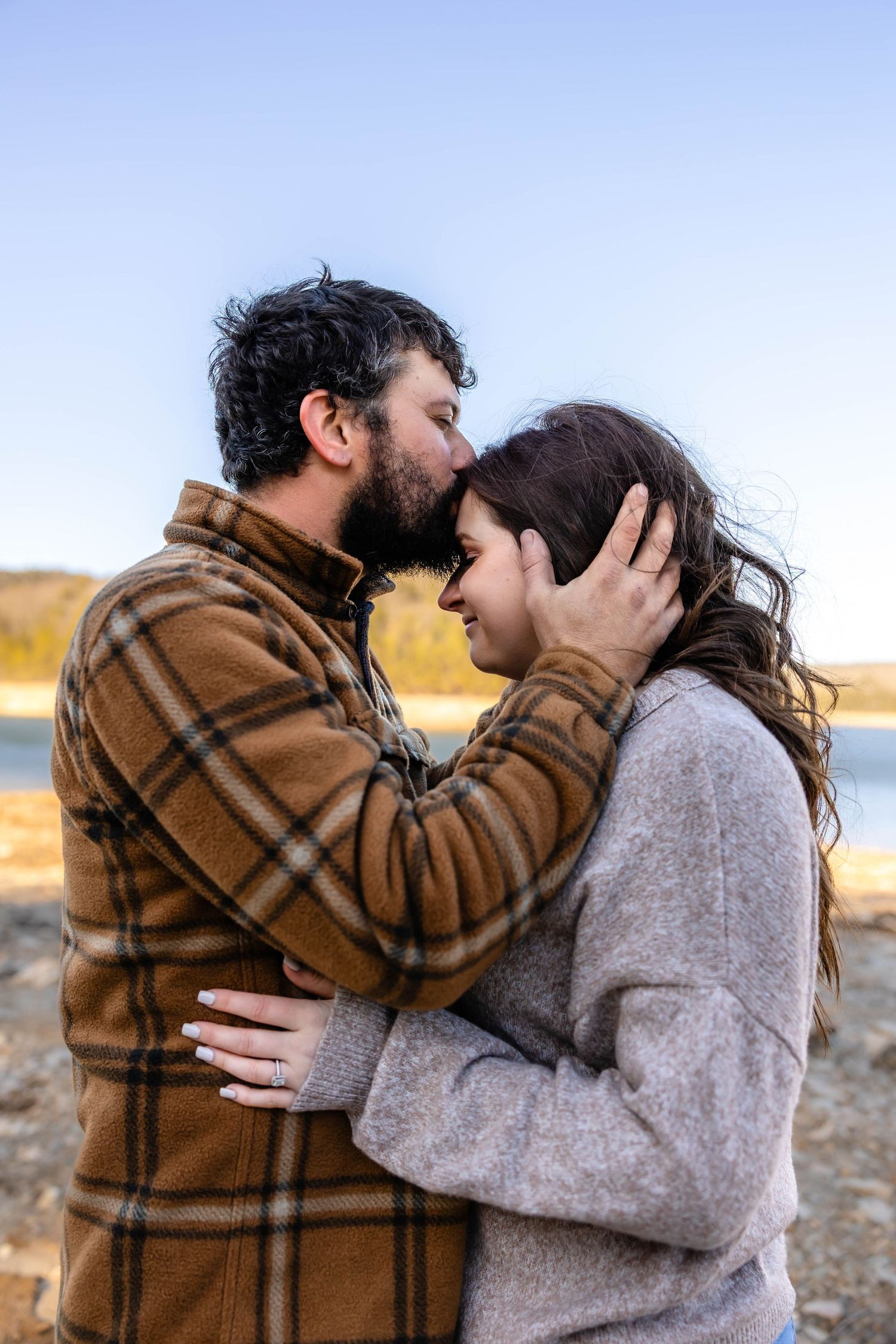 An intimate moment between a couple outdoors wearing winter clothing near a lake.