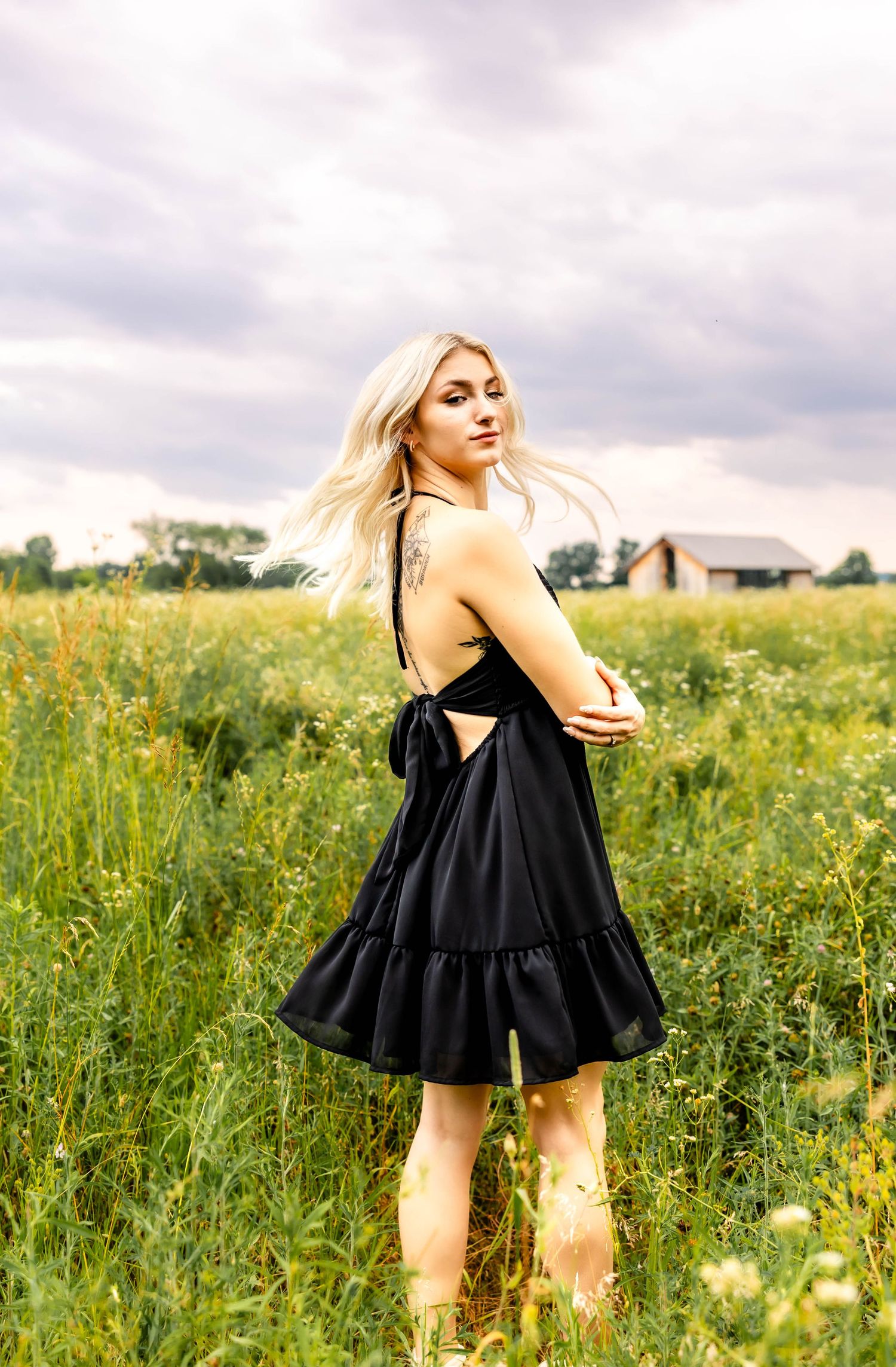 Black dress with tie back detail shown in a sunlit field of yellow wildflowers.