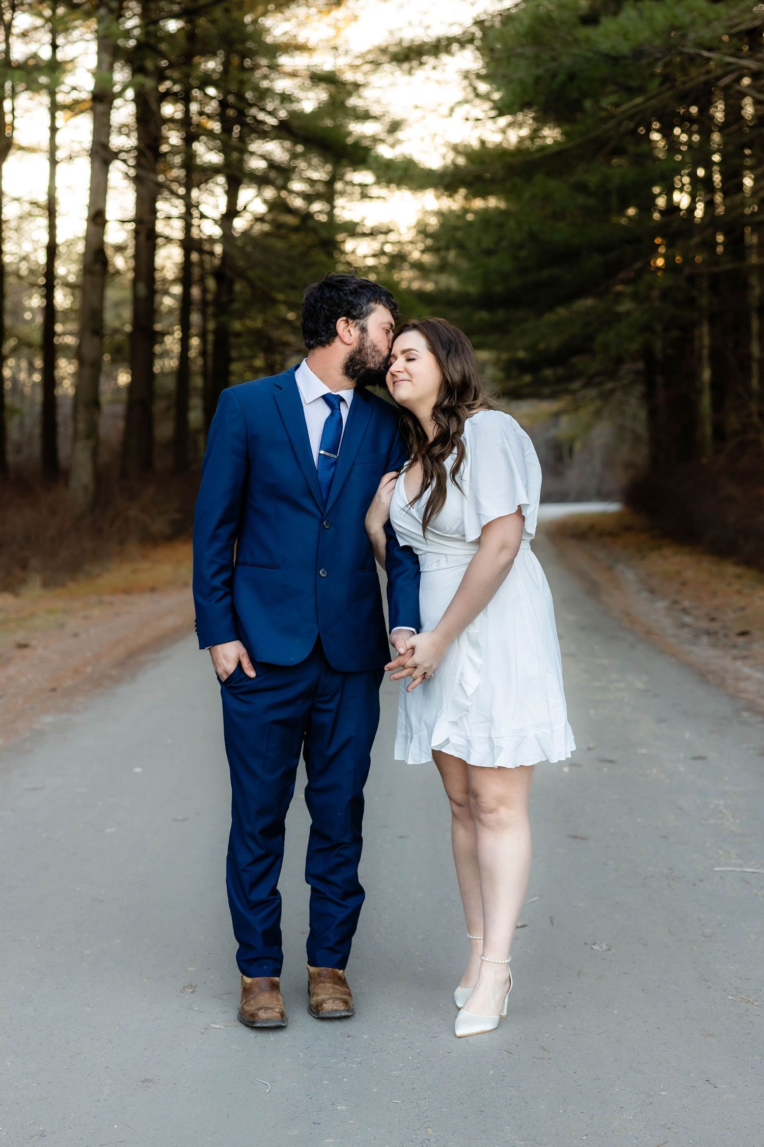 A couple shares an intimate moment on a tree-lined path at sunset.