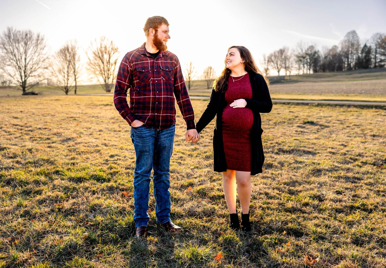 A couple stands in a golden field during sunset for their maternity photo session.