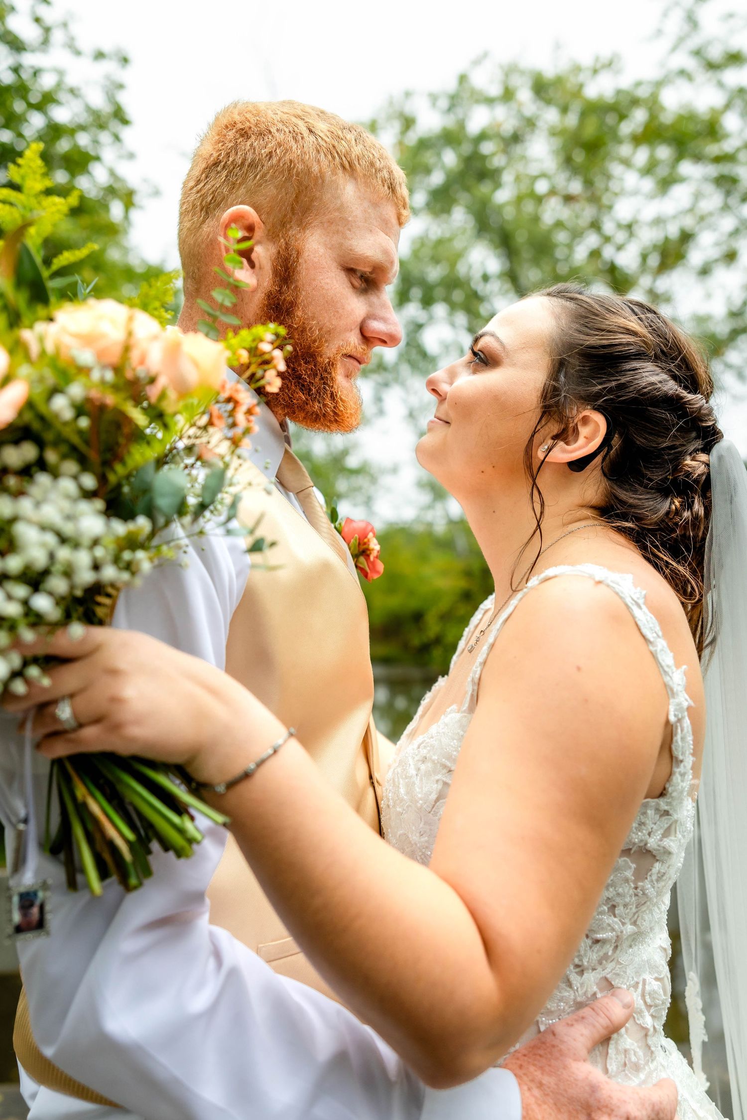 Joyful wedding couple embraces while holding a colorful bouquet outdoors.