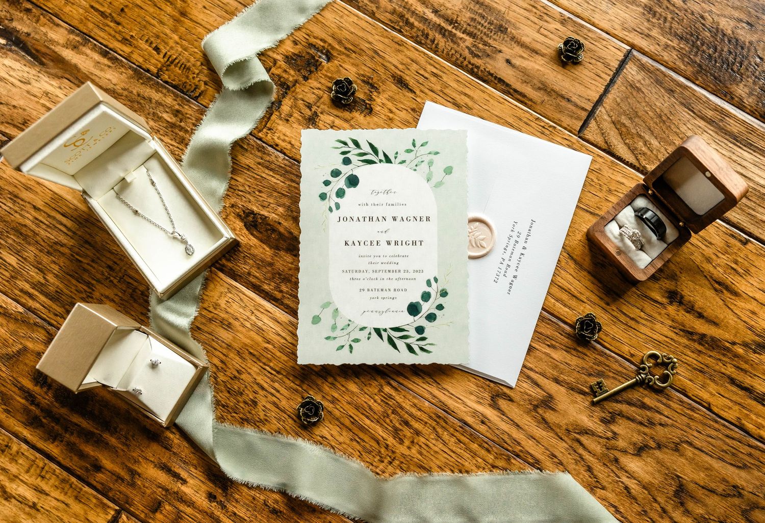 Wedding stationery suite featuring botanical design and sage ribbon laid on wooden surface.