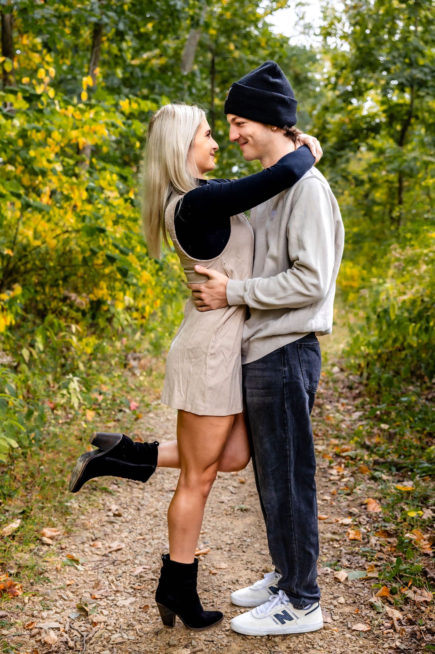 A stylish couple embraces on a forest path surrounded by fall colors.