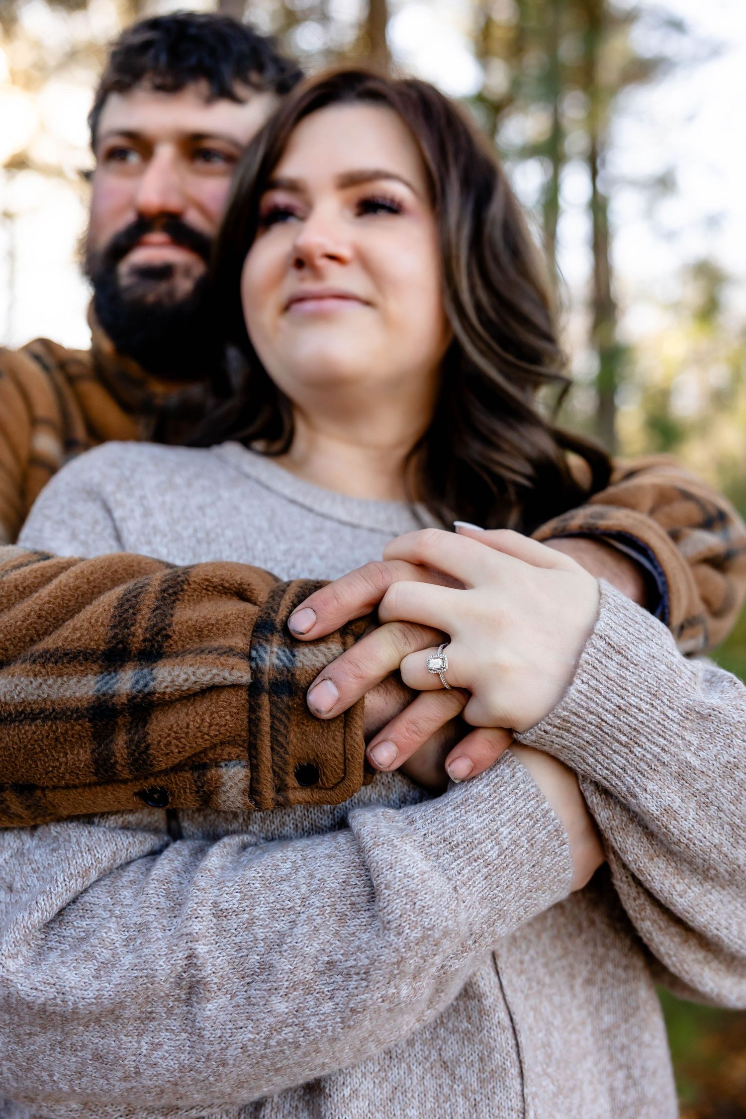 A tender moment captured between a couple showing their engagement ring in the forest.