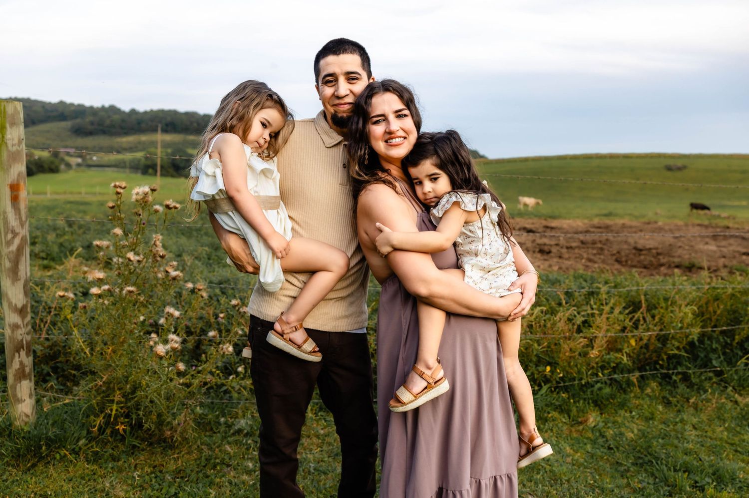 A happy family embraces while standing in a scenic rural field at sunset.