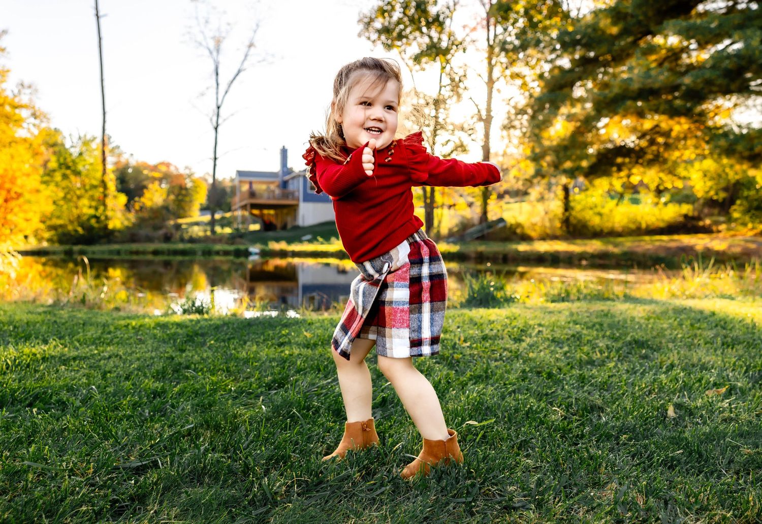 Playful child in red sweater and plaid skirt jumps with joy in an autumn garden setting with golden foliage.