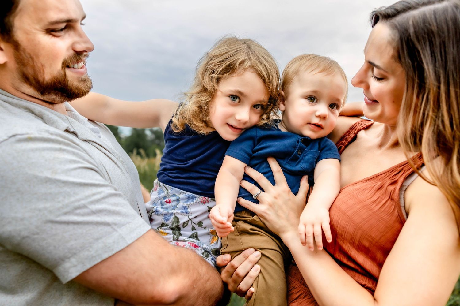 An affectionate family shares loving embraces while posing together in an outdoor field setting.