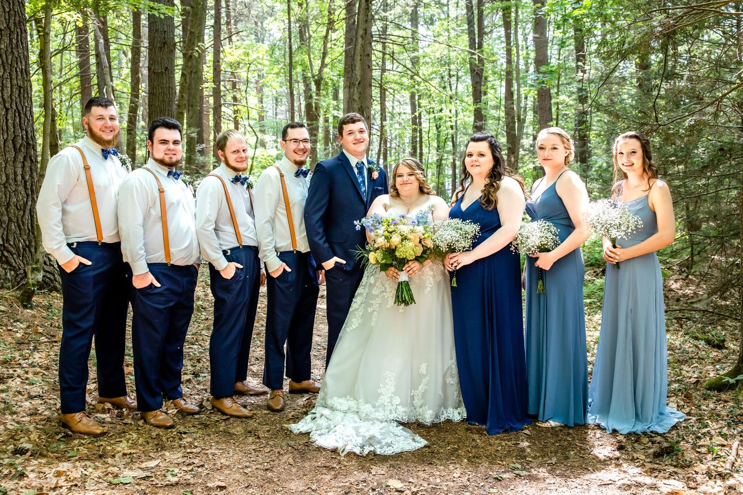 Wedding party in navy and blue attire posed together in woodland setting.