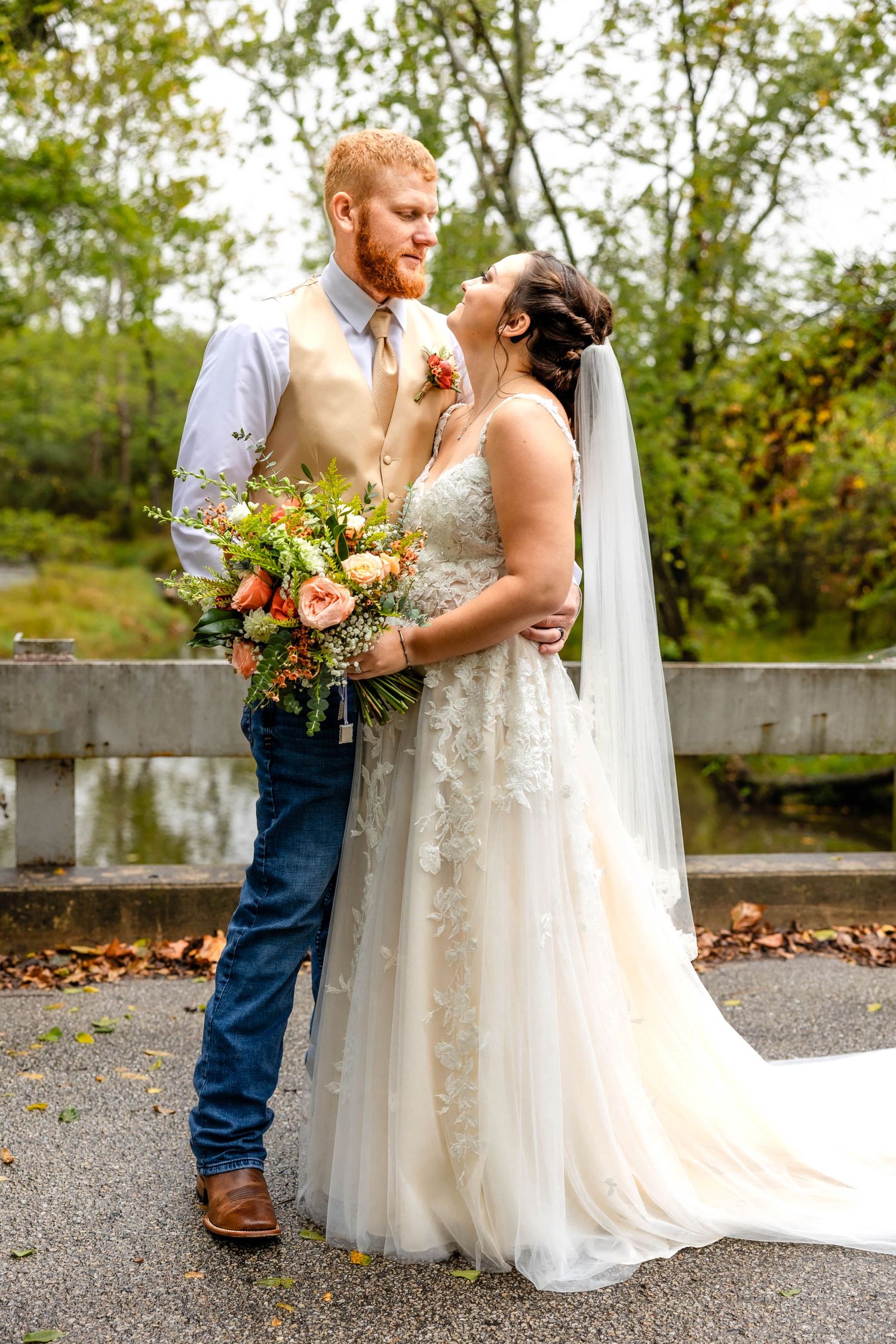 Newlywed couple shares a romantic moment outdoors with autumn foliage and a beautiful floral bouquet.