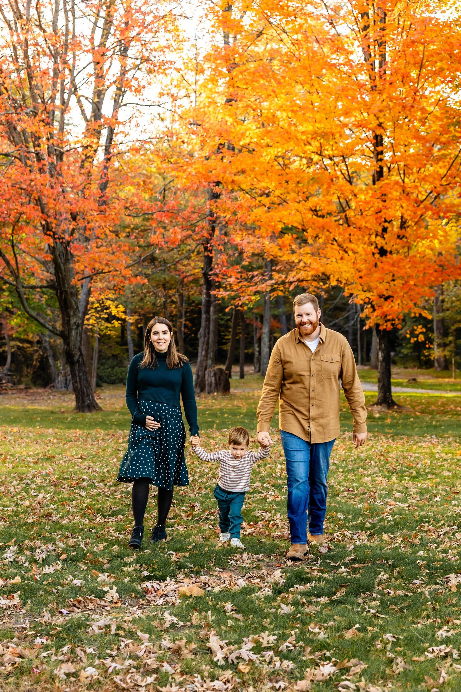 Family walking together through park with vibrant orange autumn foliage.