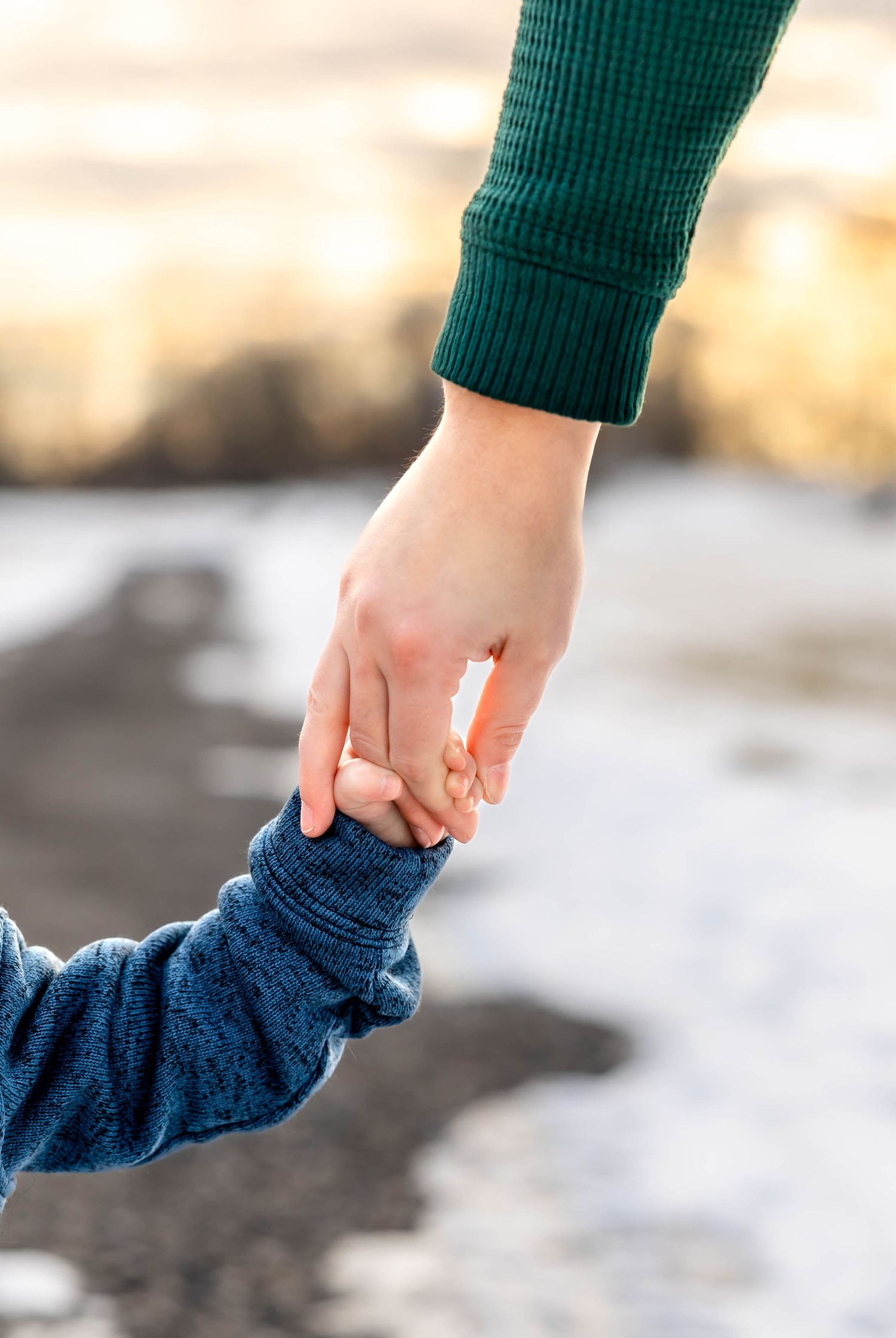 Adult and child holding hands against snowy winter background.