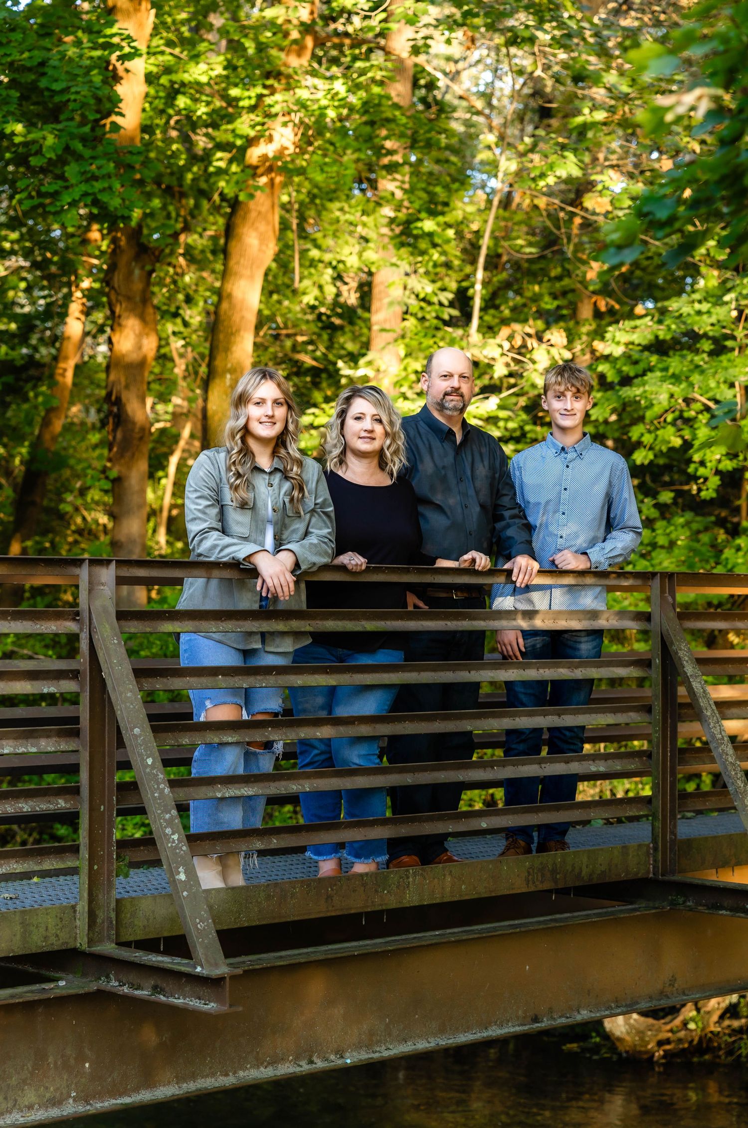 A family of four poses together on a wooden bridge in a lush forest setting during golden hour.